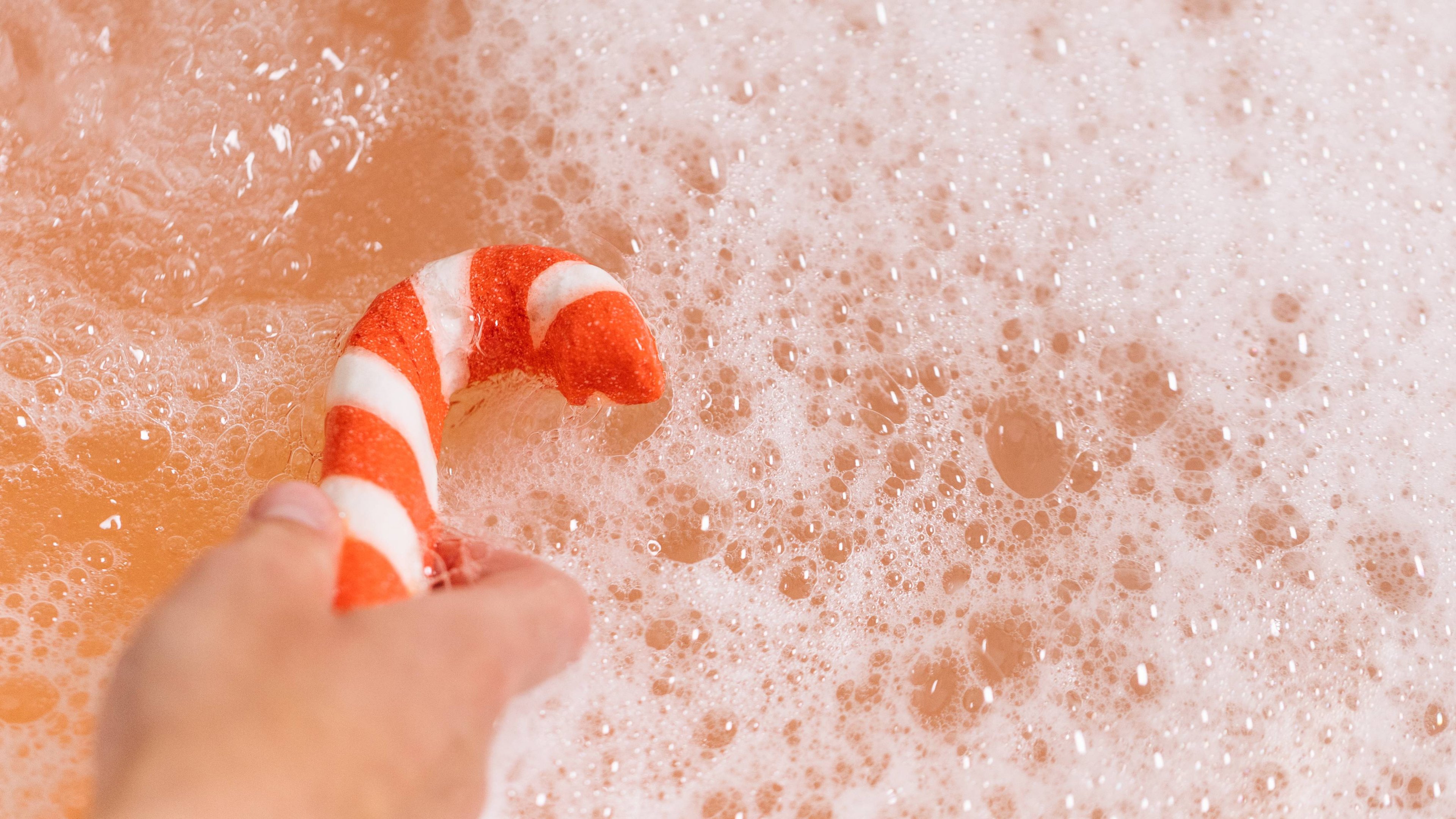 Image shows model holding the Candy Cane bubble bar in the bath water creating a calming bubble sea of orange.