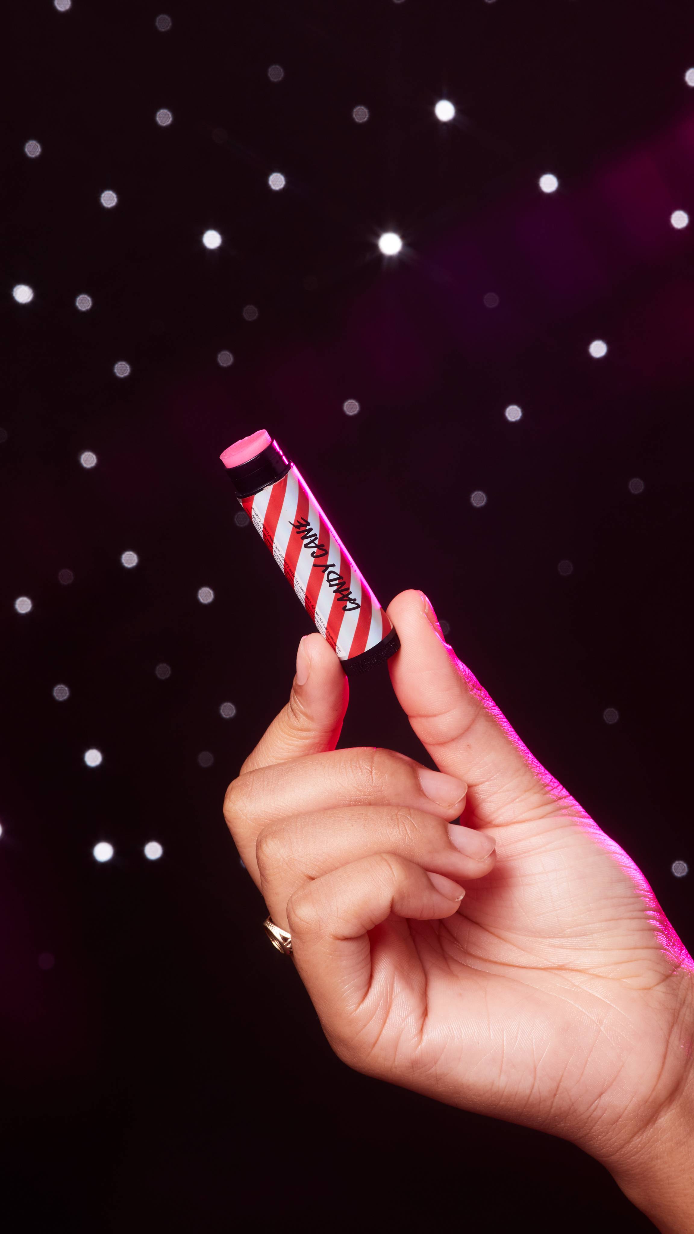 A starry backdrop shows the model's hand holding a twisted-up Candy Cane lip butter tube. 