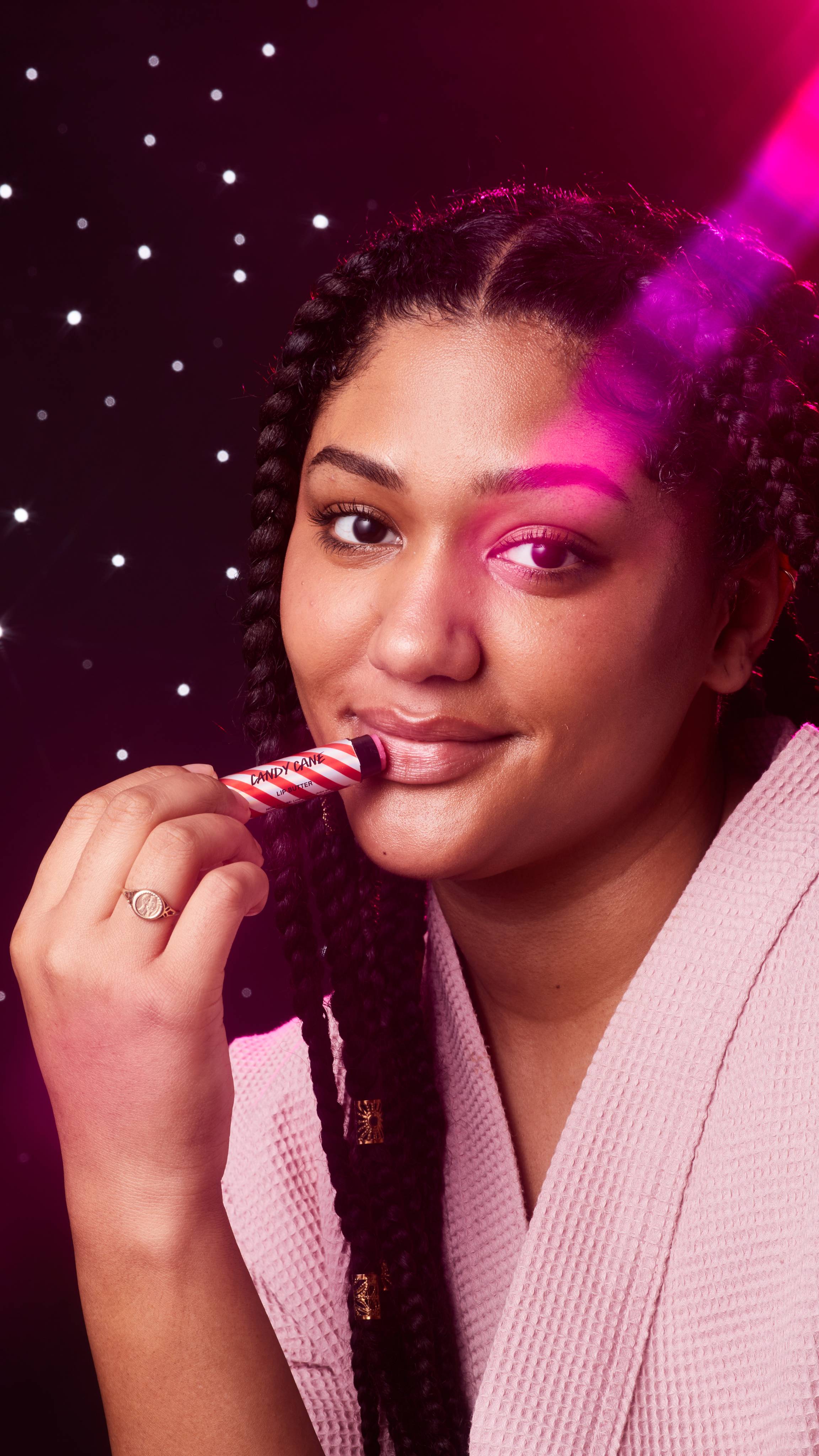 Image shows the model facing the camera with a starry backdrop as they apply the Candy Cane lip butter.