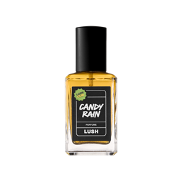 A clear glass square bottle of Candy Rain Perfume containing amber-colored liquid and a black spray top, is centered on a light grey background. The label is black with white, handwritten-style text and a small green "LUSH CLUB" sticker.