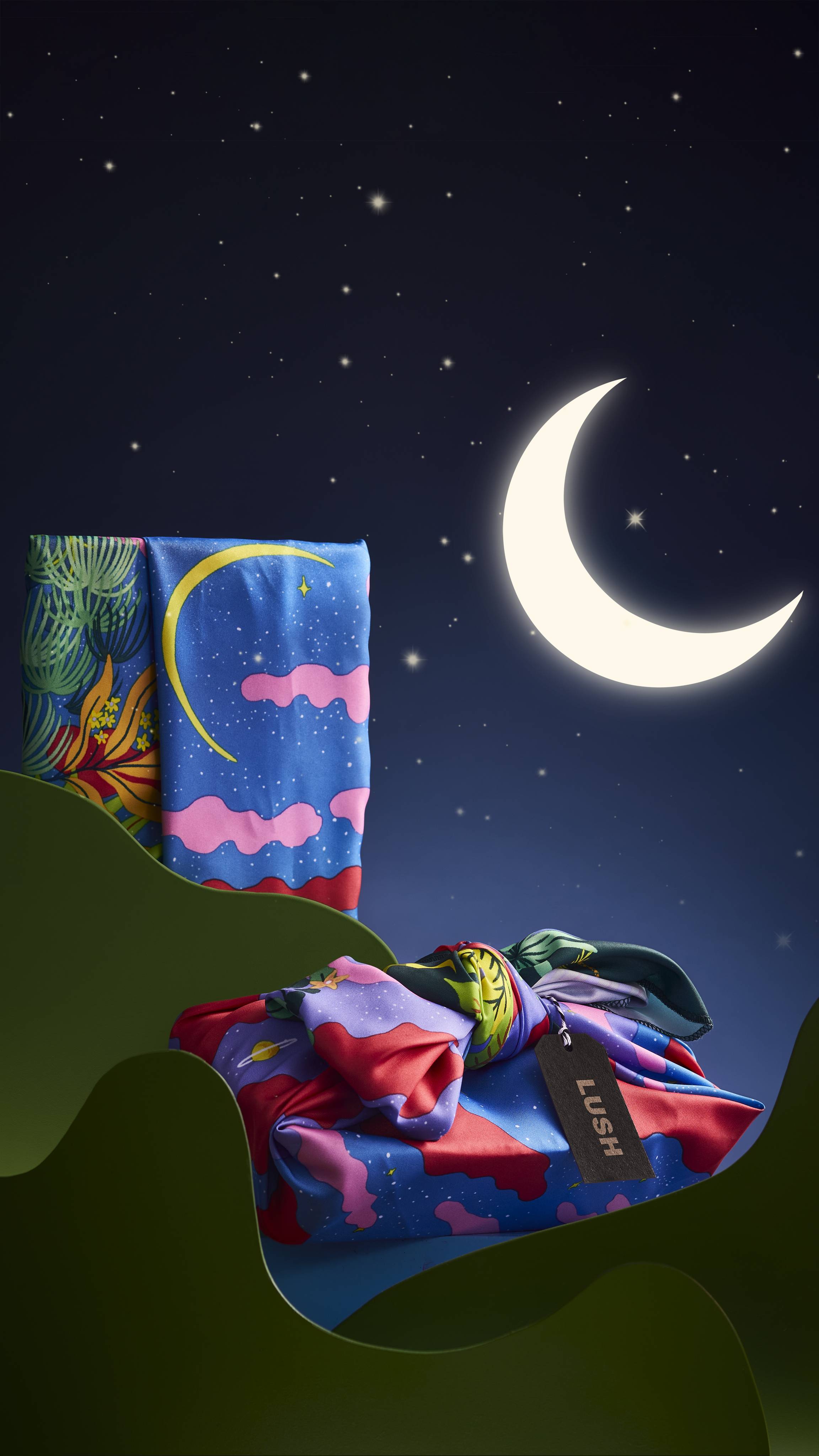 The Candy Sky knot wrap is shown two ways; folded and draped, and wrapped around a gift box. Both wraps are on a wavy green stand on a starry background with a crescent moon.