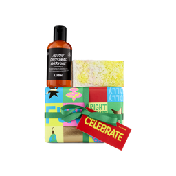 A festive Lush "Celebrate" gift set. A brightly colored, pop-art-style gift box is wrapped with a green ribbon and a red tag. The set is topped with a bottle of "Merry Christmas Everyone" shower gel and a white-and-yellow solid bath product.