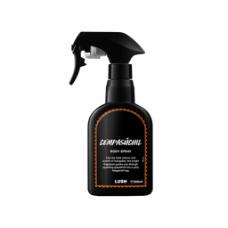 Cempasúchil. A recycled black plastic body spray bottle with a trigger nozzle stands upright. It features a black label with intricate orange border designs and white text.