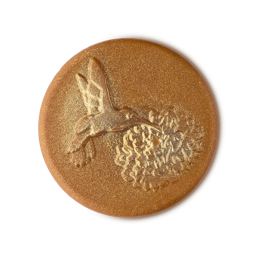 Cempasúchil Soap. The image shows a round, golden, disc-shaped soap with an embossed hummingbird hovering over a flower. It has a strong glittery lustre and a slightly textured surface.