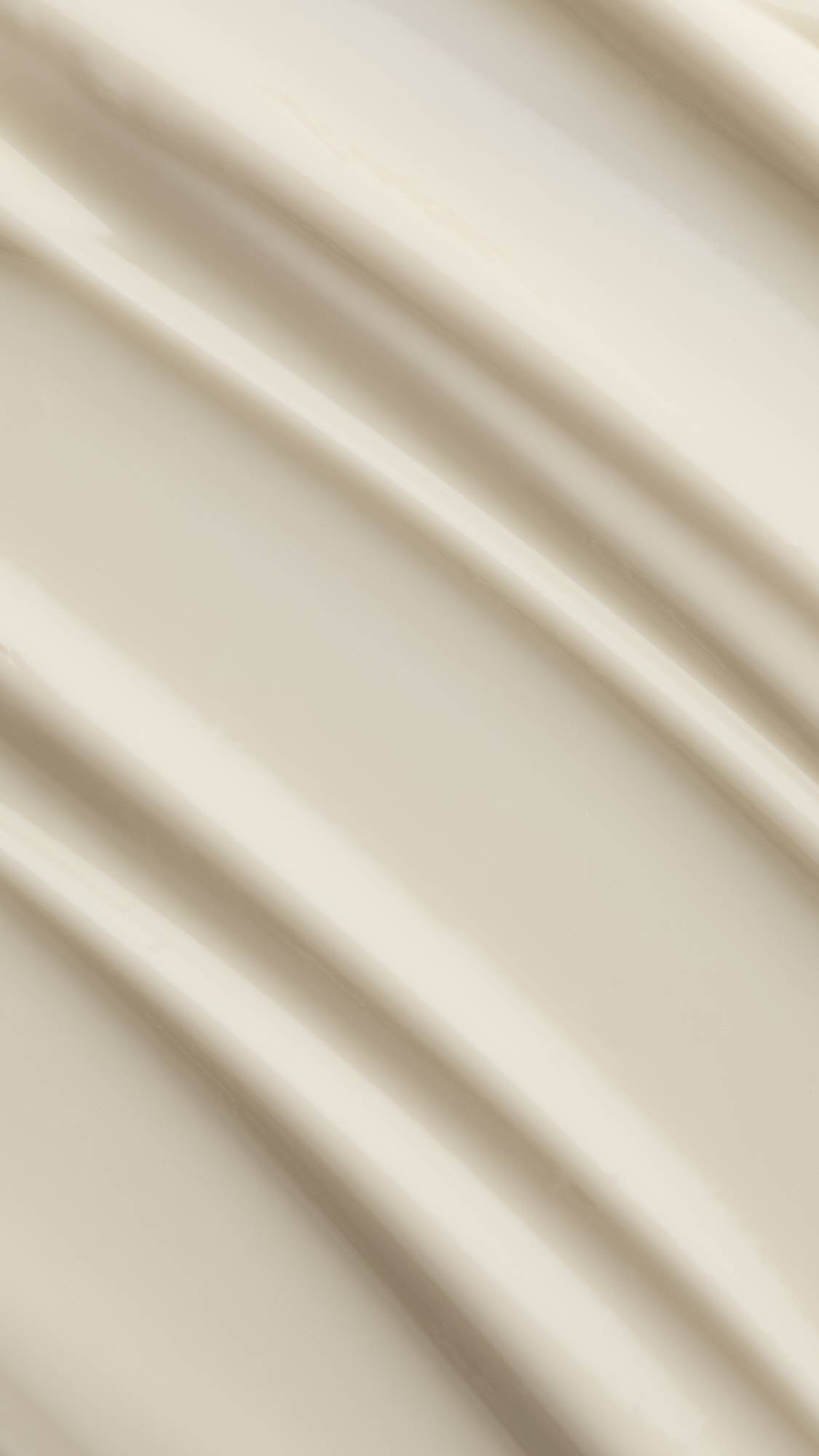 A macro close-up texture shot of rich, creamy off-white body lotion spread in smooth, soft diagonal ridges across the frame.