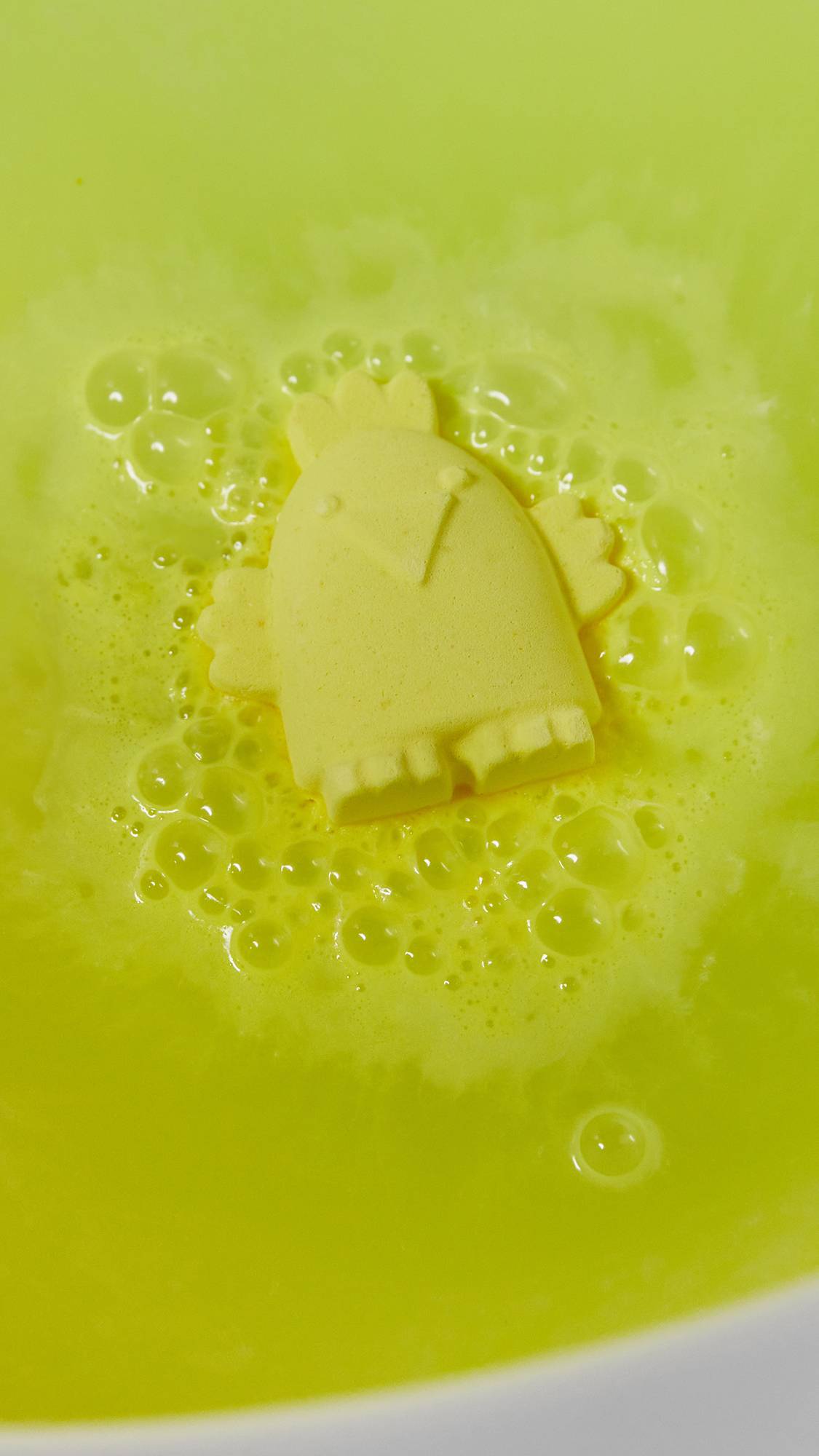 The Cheep Cheep bath bomb sits on top of the water fizzing bright, neon yellow foam.