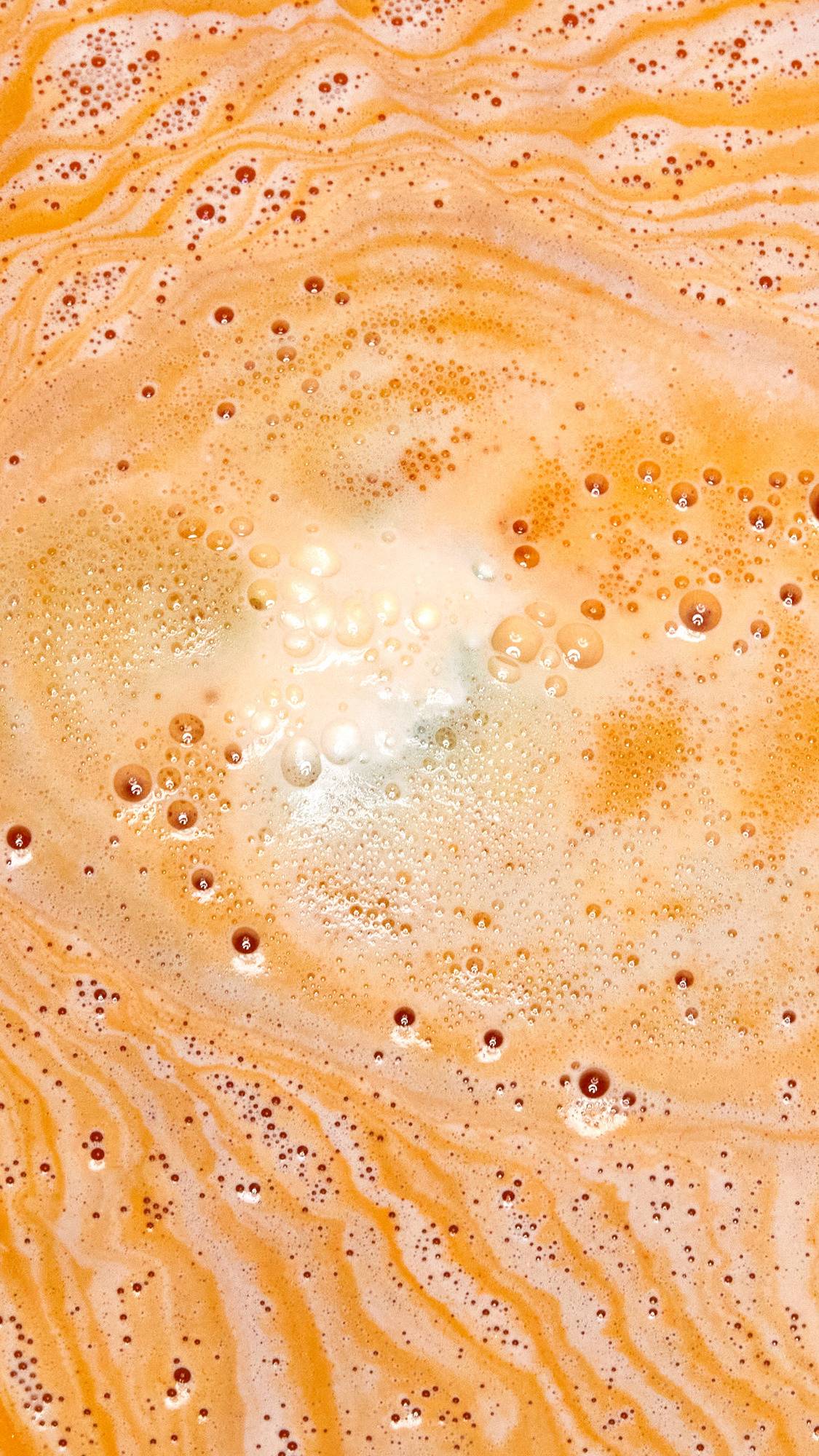 The Chelsea Morning bath bomb is dissolving in the bath water creating layers of foamy, bright orange ripples.