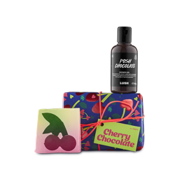 Cherry Chocolate. A small, rectangular gift box wrapped in blue, cherry-patterned paper and tied with orange string. A bottle of Posh Chocolate shower gel and Cherry On Top slap slice sit around the box. 