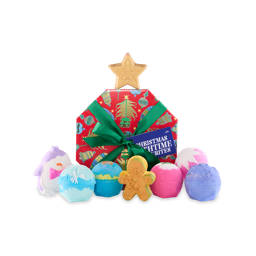 Christmas Bathtime Favourites. An octagonal-shaped gift box designed with a red background and illustrations of baubles, bells and Christmas trees, tied with a green ribbon and gift tag. Eight Christmas-themed bath bombs sit on and around the box. 
