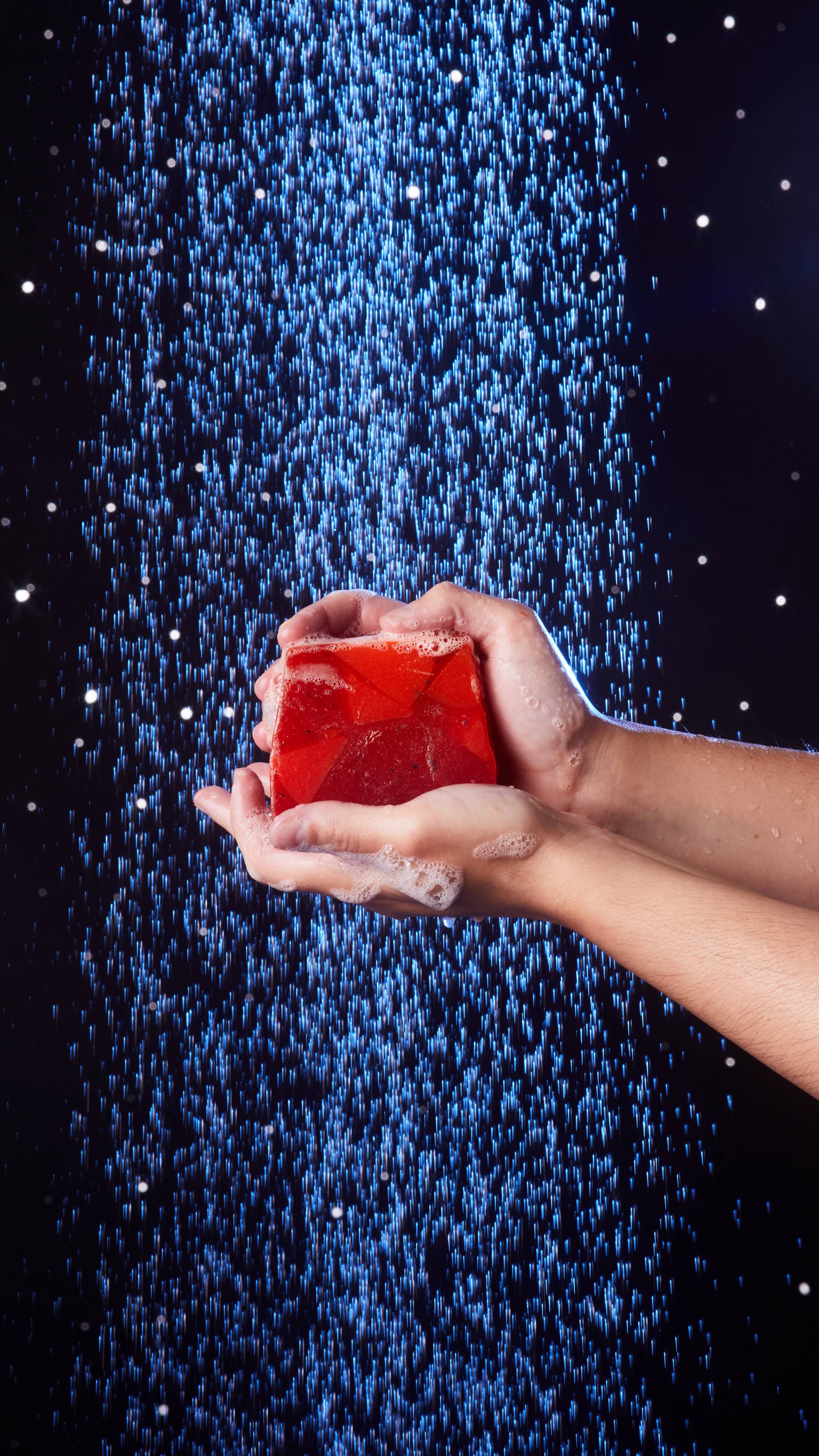Model holds the Christmas Cranberry soap with both hands under the shower as it makes a bubbly lather. 