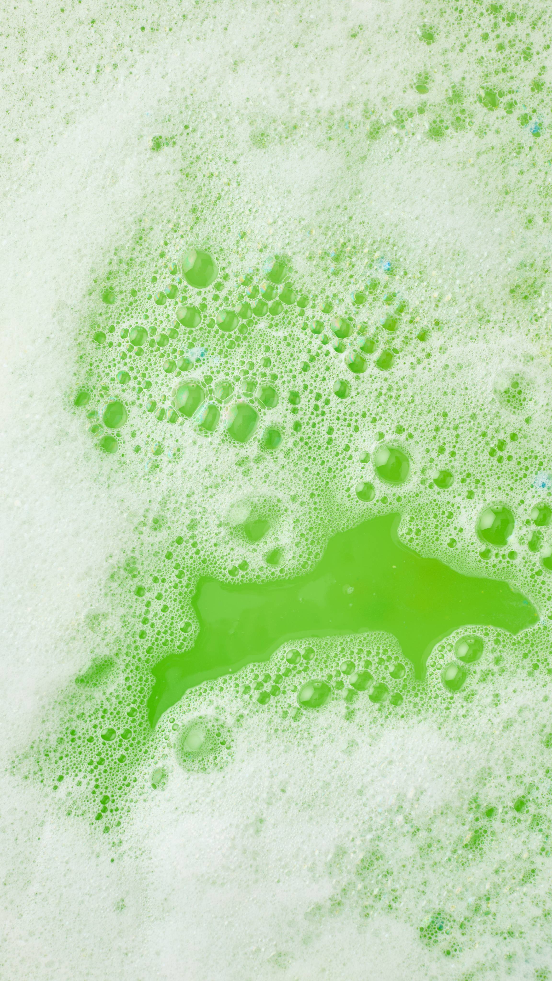 The image shows an aerial view of the bath after using the yellow moon and blue sky Christmas Eve bubble bar. The water has been turned a bright green colour, bordered with thick mountains of white bubbles. 