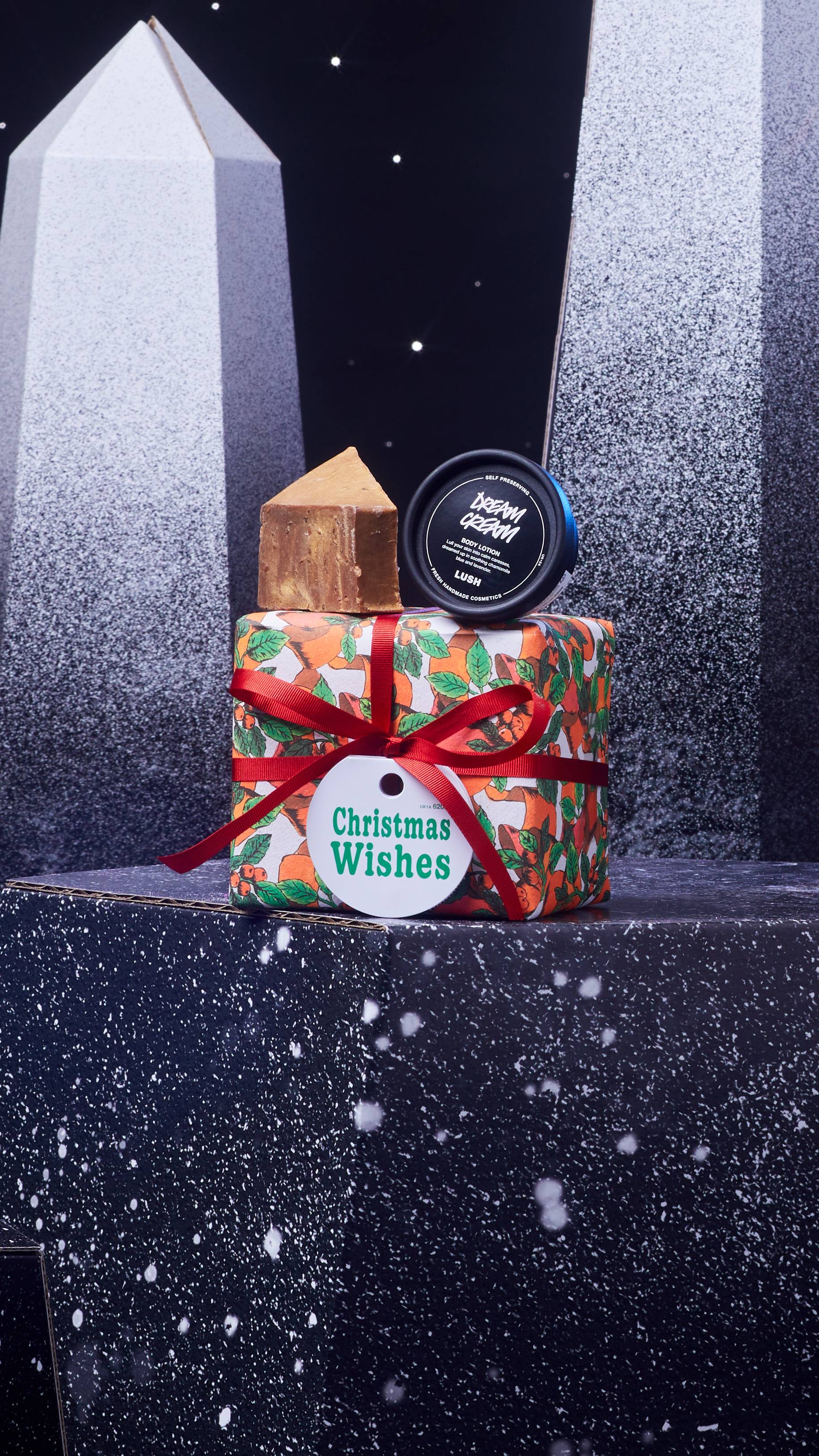 Christmas Wishes gift box and two included products are on a dark chromatic platform among geometric shapes. 