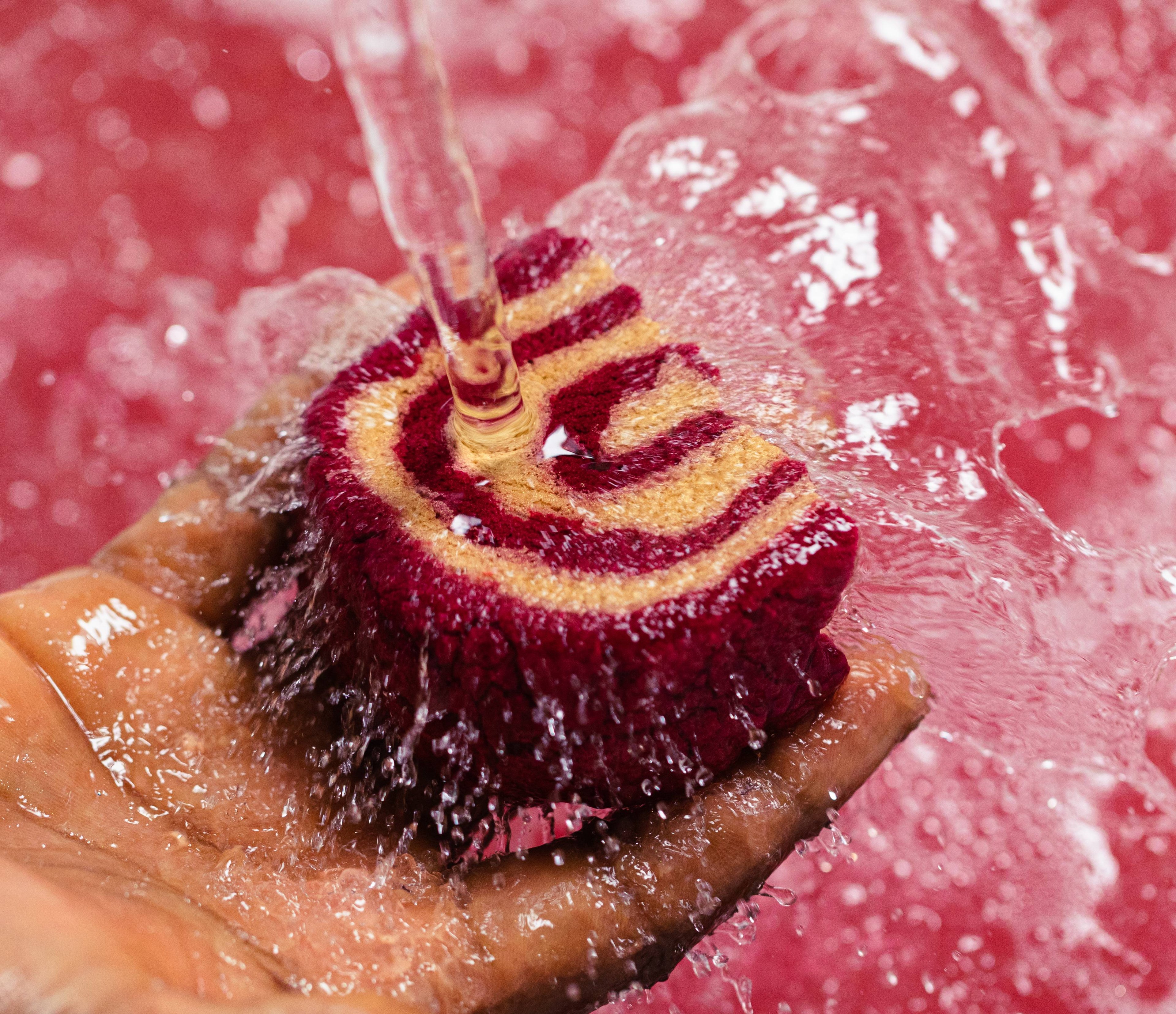 Image shows model holding half of the Cinnamon Roll bubble bar under running water with a sea of pink below. 