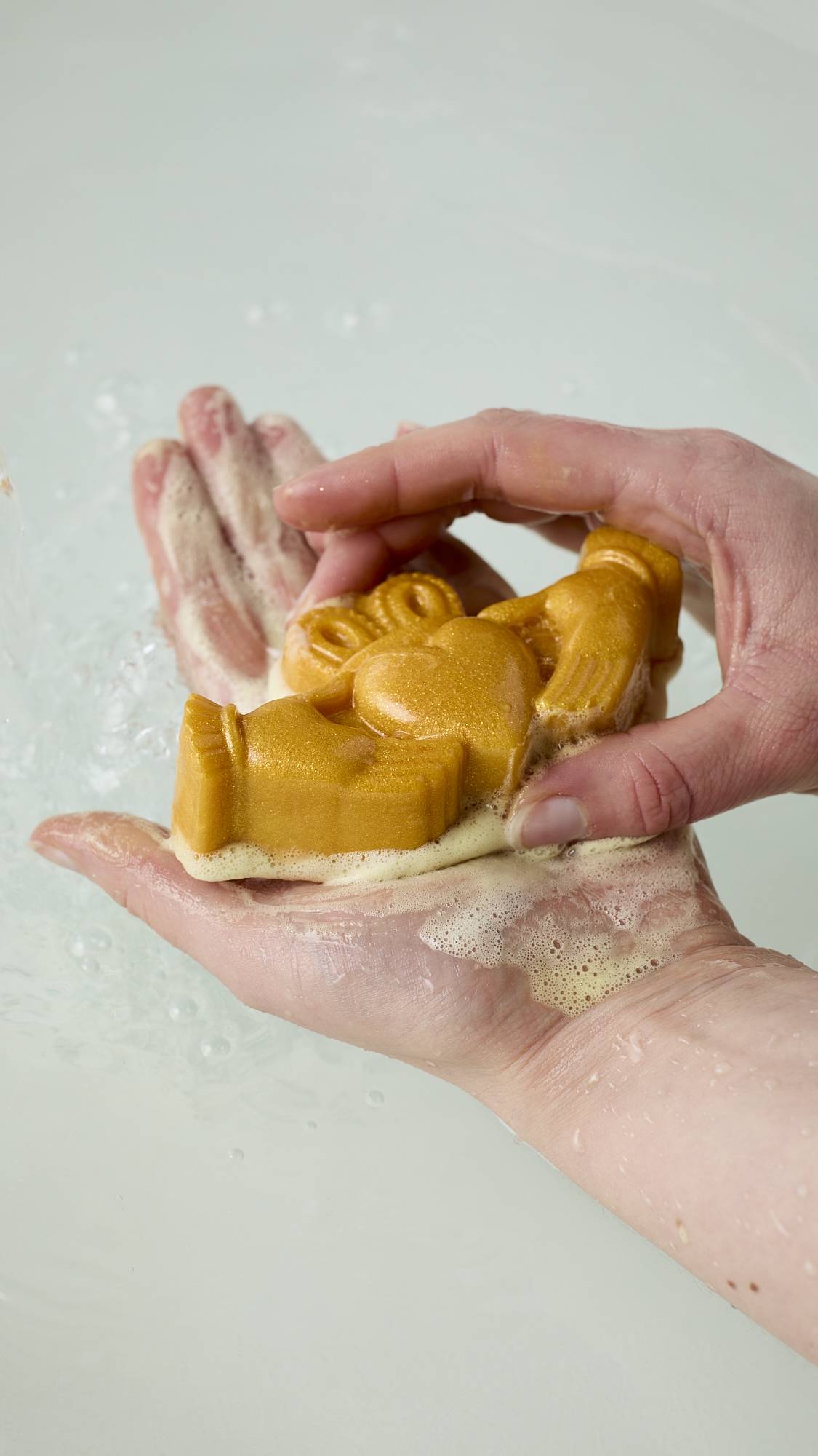 The image shows the model's hands holding the traditional Claddagh-shaped soap after lathering it up with water in their palm, creating a delicate, golden, soapy lather over their skin.