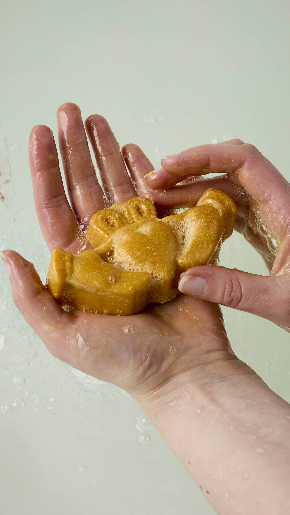 The image shows the model's hands holding the traditional Claddagh-shaped soap after lathering it up with water in their palm, creating a delicate, golden, soapy lather over their skin.