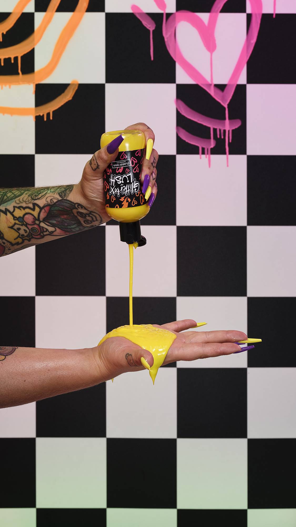 Image shows the model squeezing the bottle of bright yellow shower gel onto their hand in front of a checkered background.