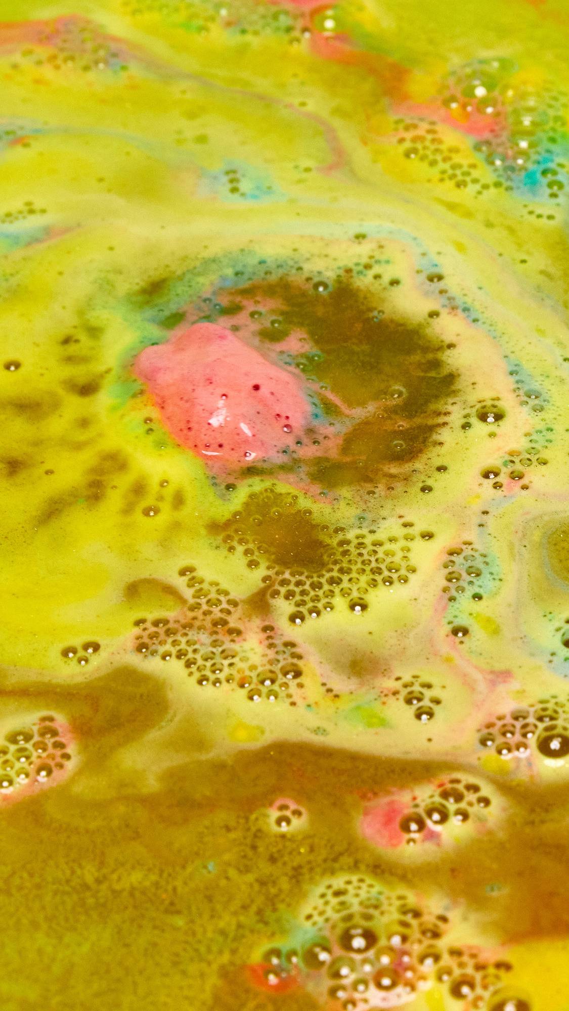 The Crackle bath bomb is slowly dissolving among shimmering golden waters with ribbons of blue and red throughout. 