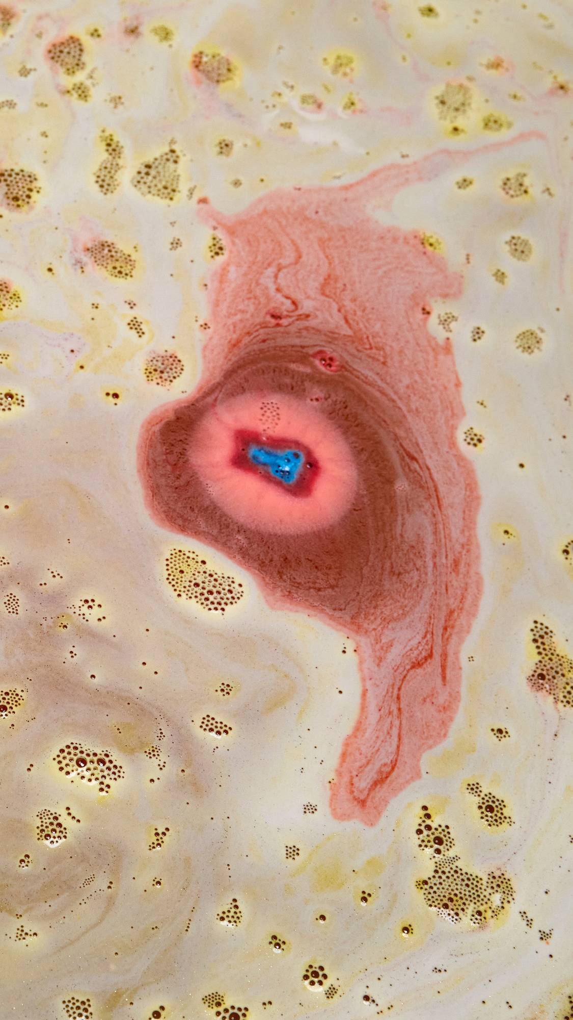 The Crackle bath bomb has almost fully dissolved in the bath leaving behind a sea of deep golden, shimmering water. The centre is a deep red colour with a pop of blue.