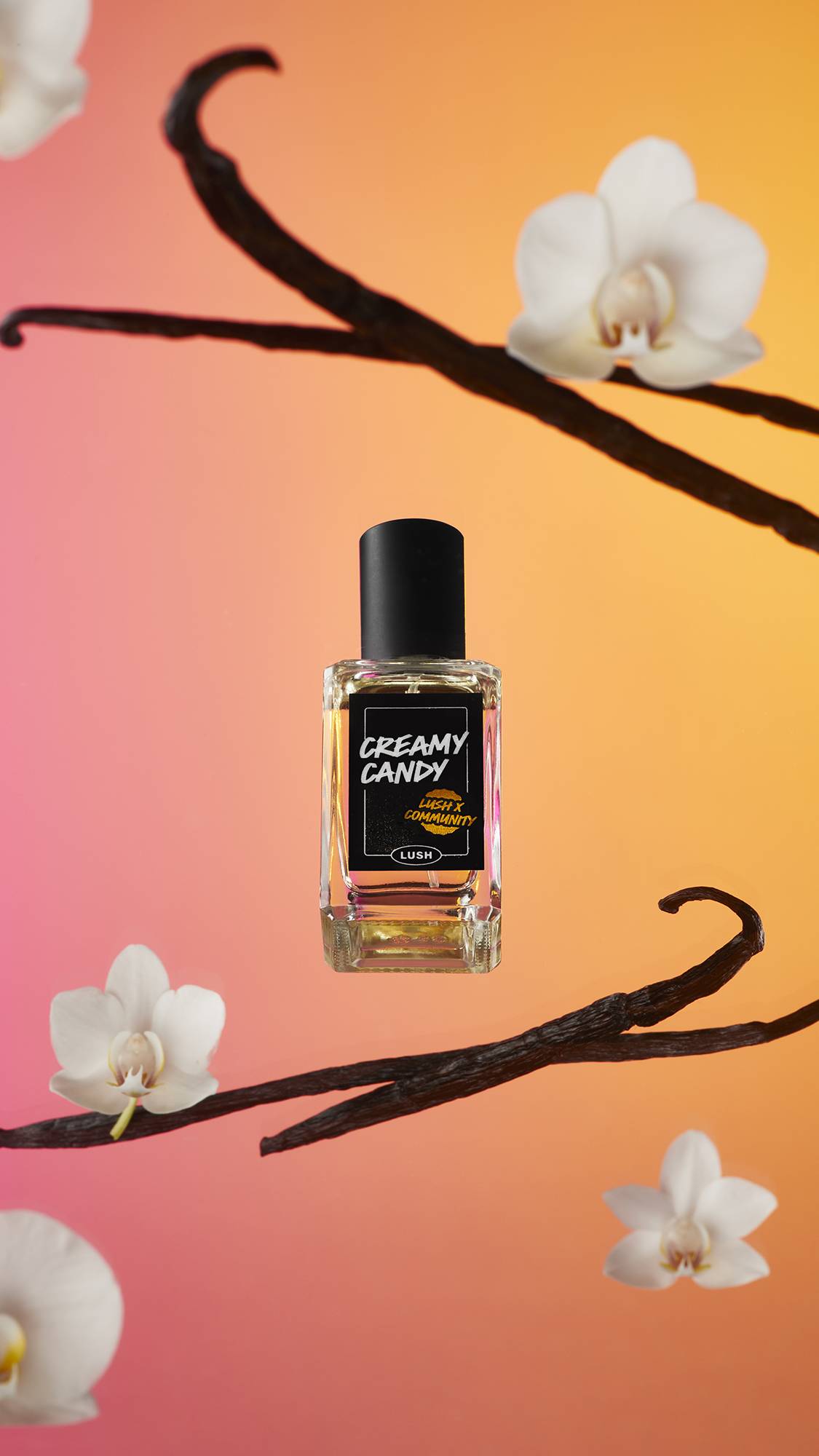 The Creamy Candy perfume bottle is in front of a pink and orange background surrounded by vanilla pods and flowers.