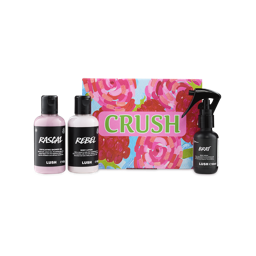 A LUSH Crush gift set featuring a brightly colored box with pink roses, next to three small black and white bottles: "Rascal" exfoliating shower gel, "Rebel" body lotion, and "Brat" body spray.