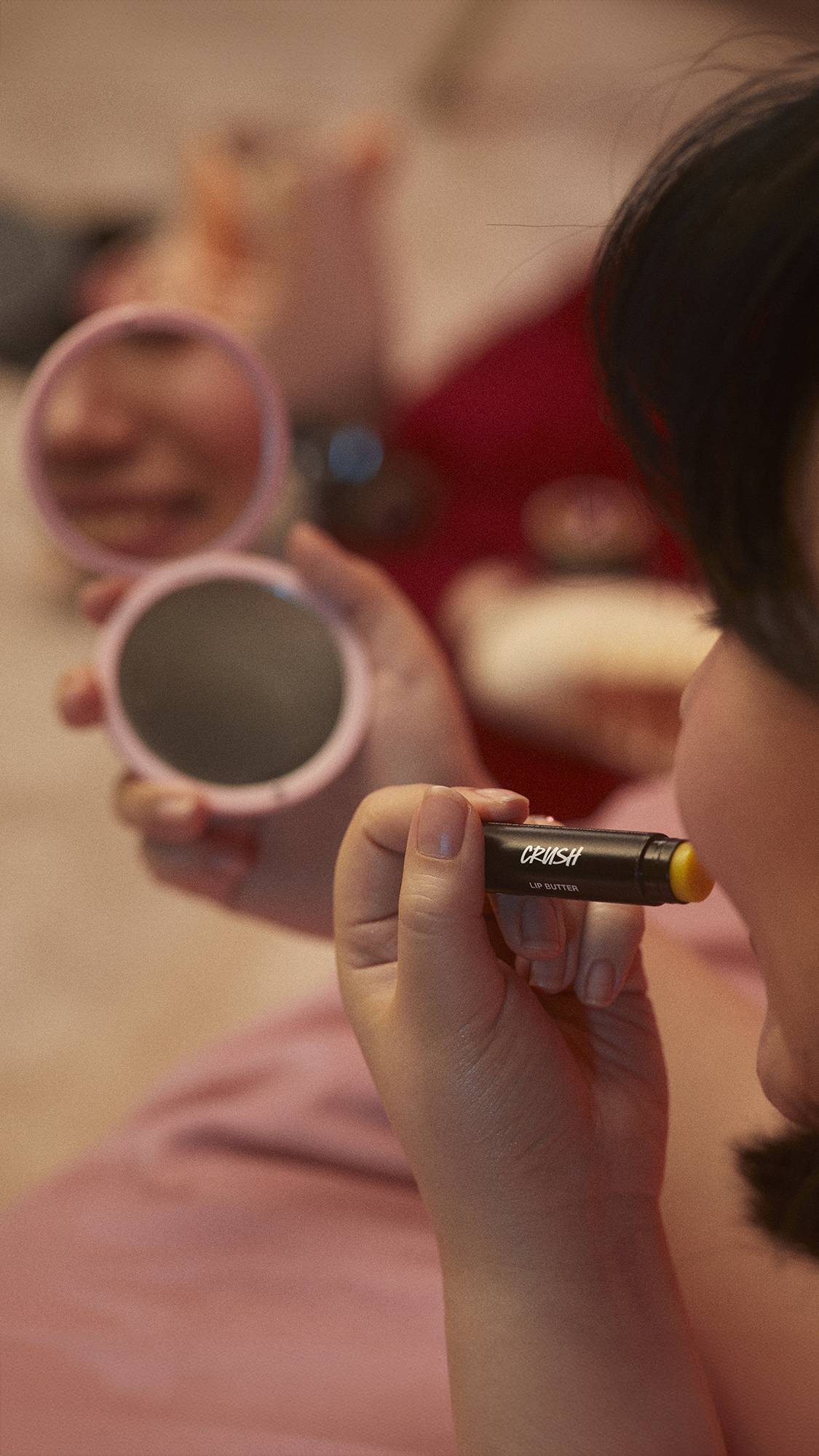 The image shows a super close-up of the model's hand as they are holding the Crush lip butter.