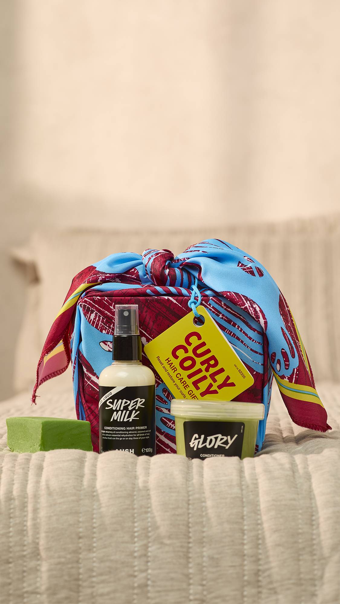 A close-up of the Curly Coily wrapped haircare gift set on the foot of the bed with the three haircare products sitting in front. 
