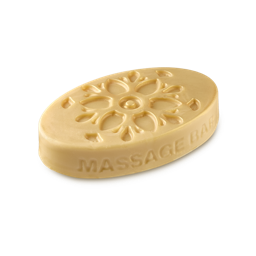 Delight And Decadence. A smooth, pale cream, oval-shaped solid massage bar. Its upper surface features a large, embossed floral pattern, with the text 'MASSAGE BAR' along its side, coated in a subtle gold lustre.