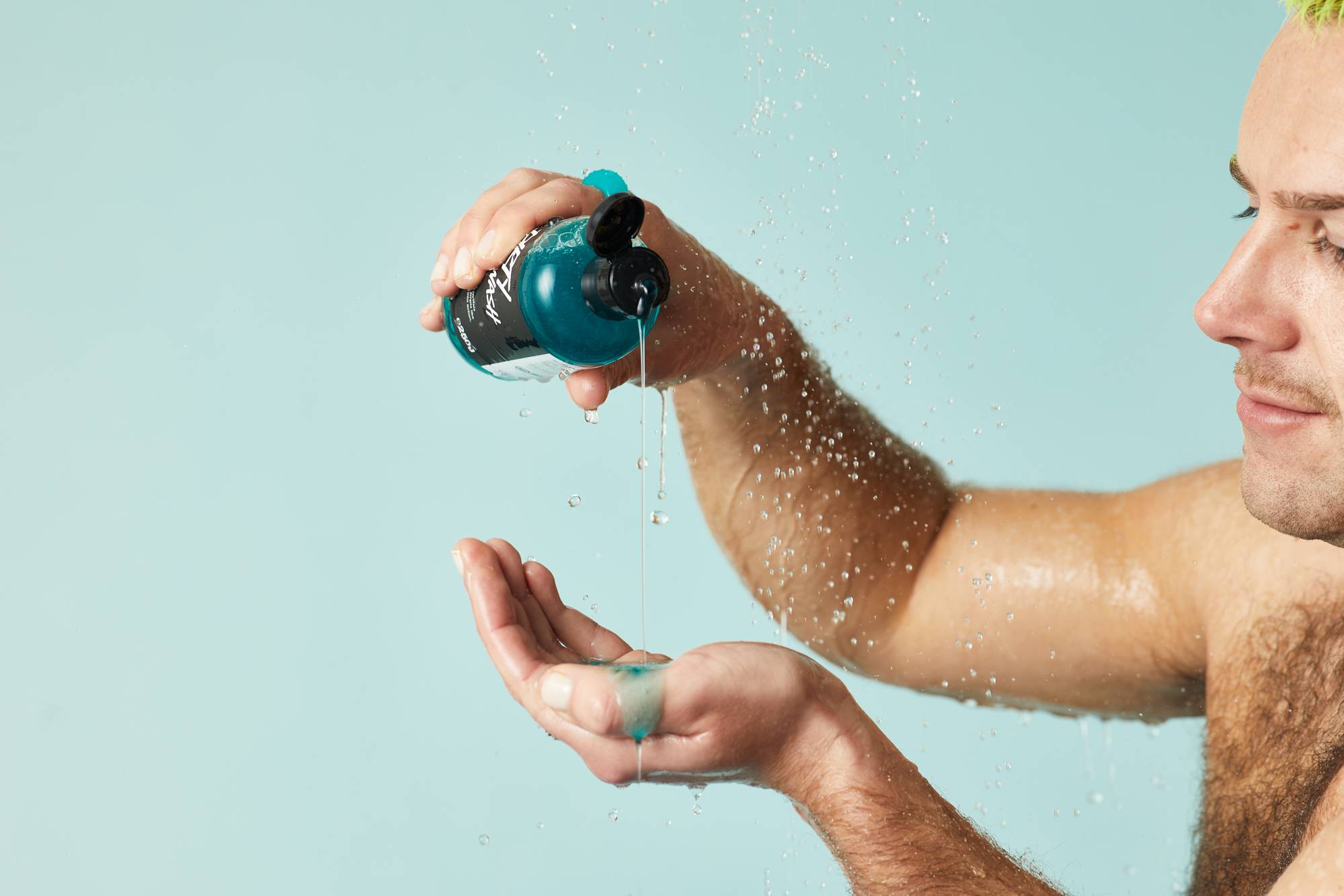 A person pours blue Dirty Spirngwash shower gel into their hand as water droplets fall.