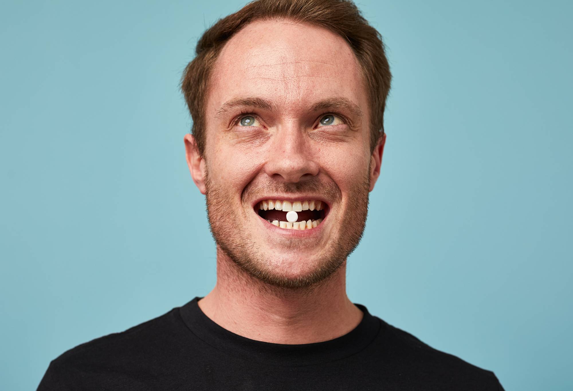 A person shows off their teeth and holds a small white Dirty toothpaste tab between their front teeth.