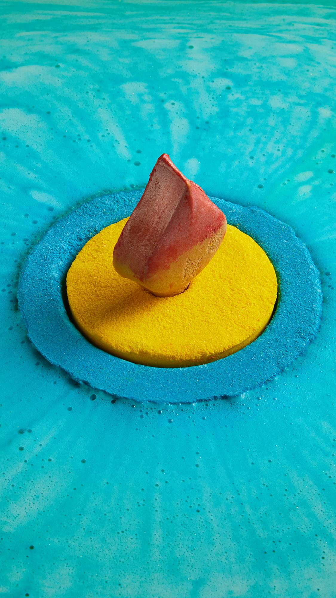 Diya bath bomb floats atop the water surrounded by vivid blue foam. The yellow centre and solid oil flame are still intact.