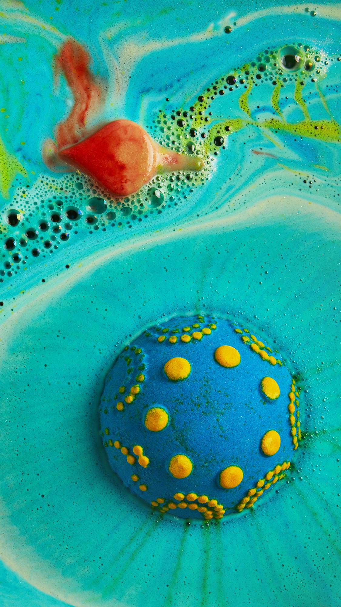 Diya bath bomb's lower segment is floating upside down, showing yellow details as the oil flame melts beside on a sea of foam.