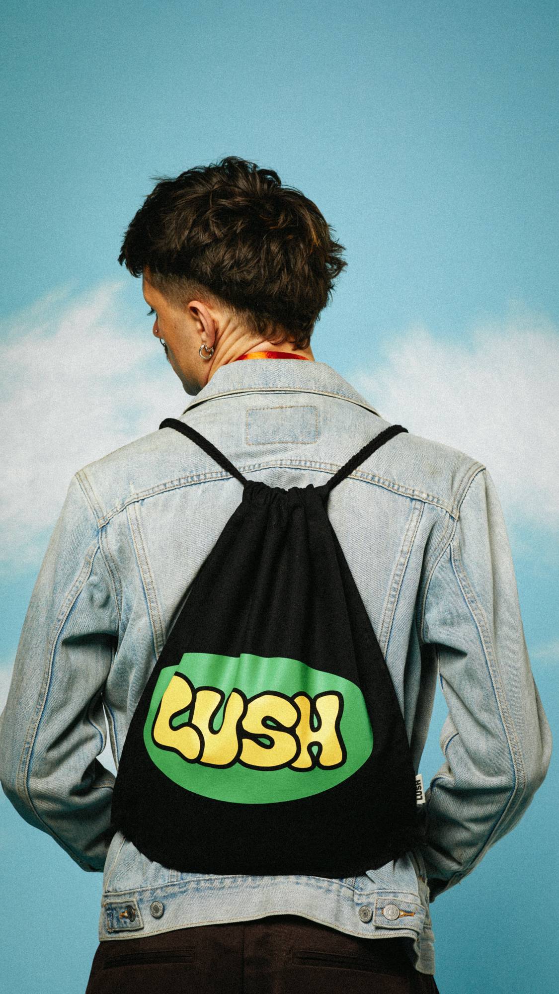 Image shows the model facing away, wearing a denim jacket as they wear the Retro Bubble drawstring bag on their back.