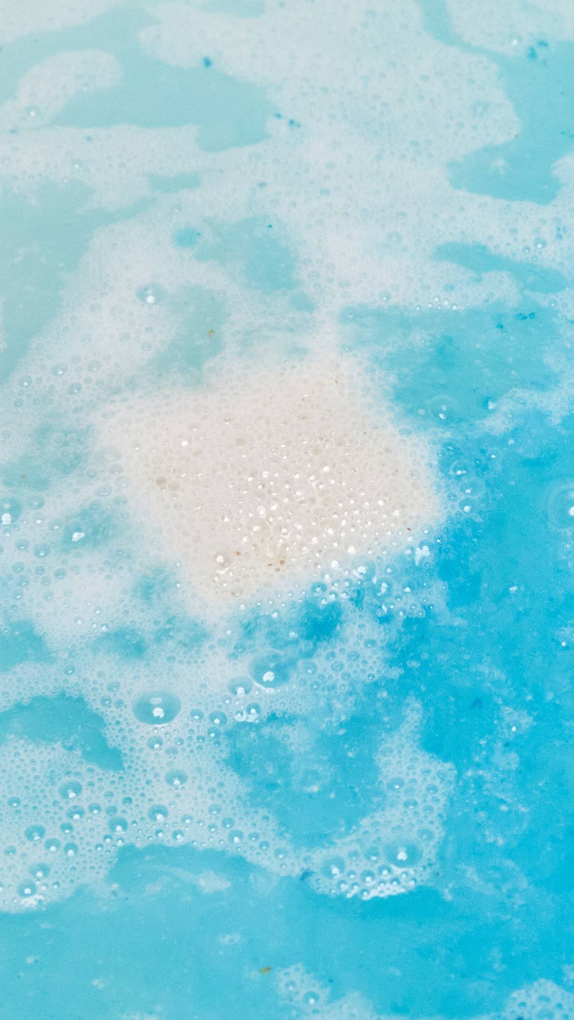 The Dream Cream Epsom salt bath bomb has dissolved leaving clear, turquoise water with a delicate dusting of foam on the surface. 