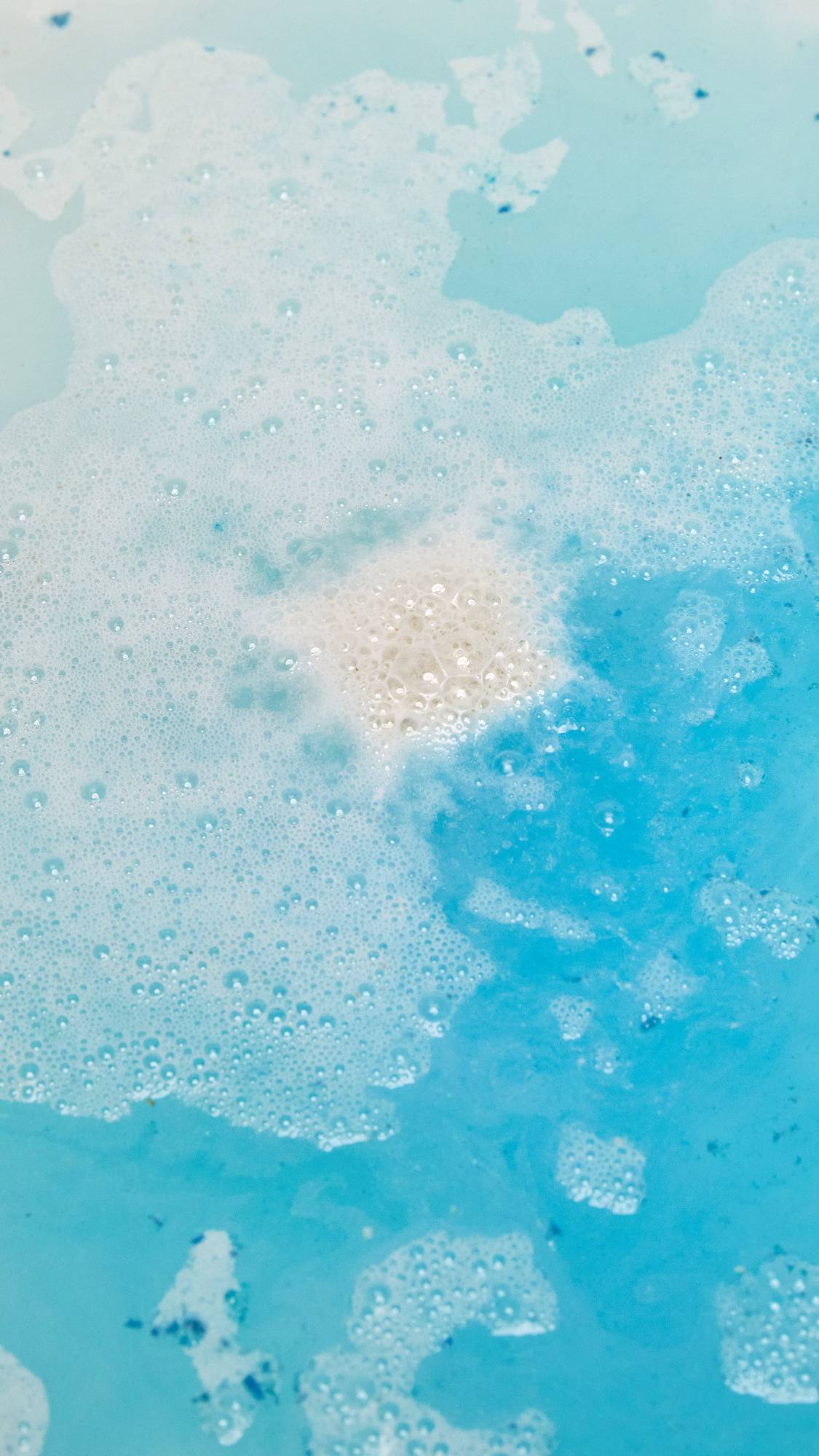 The Dream Cream Epsom salt bath bomb has dissolved leaving clear, turquoise water with a delicate dusting of foam on the surface. 