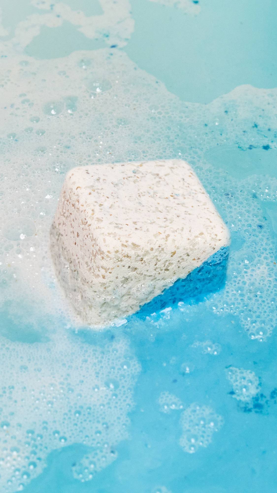 The Dream Cream bath bomb has been placed in the bath water and is giving off delicate swirls of clear blue water and sweet sea foam.