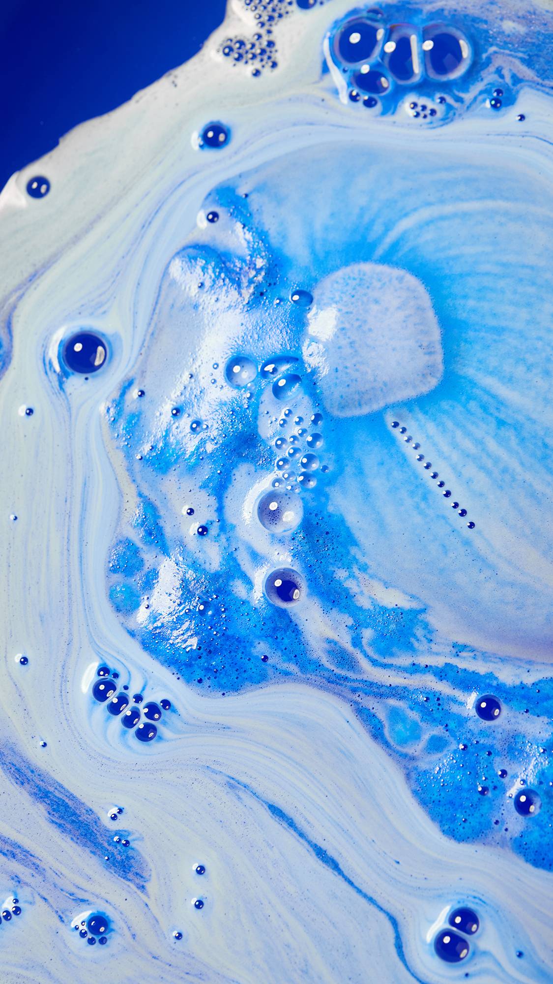 An aerial view of the bath water after using the Dreidel, Dreidel, Dreidel bath bomb. There is an elegant swirling pattern of light and dark blues with hints of deep indigo bath water below. 