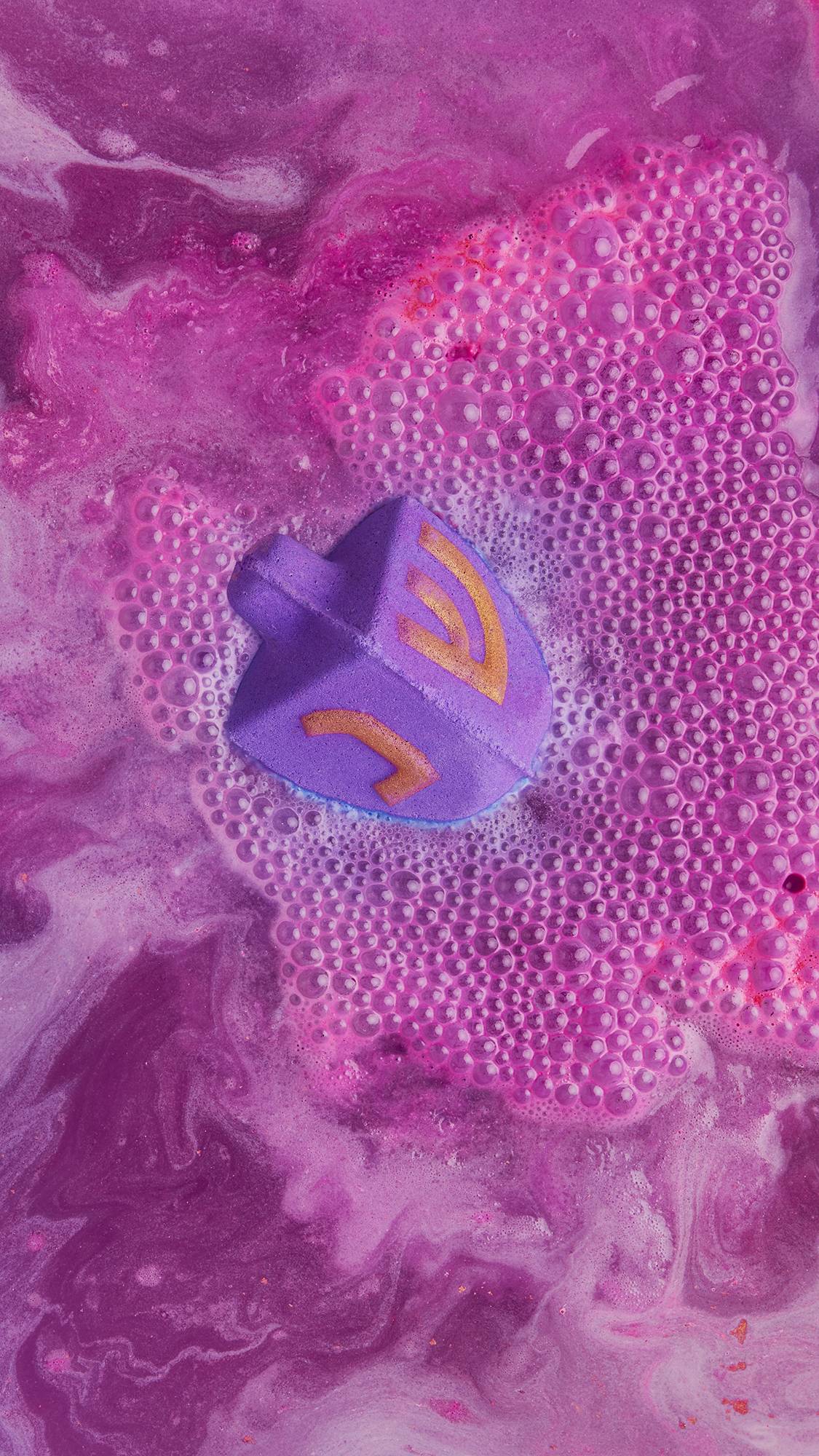 Dreidel, Dreidel, Dreidel bath bomb dissolves into the bath water as it fizzes with vivid pink and purple swirling foam.