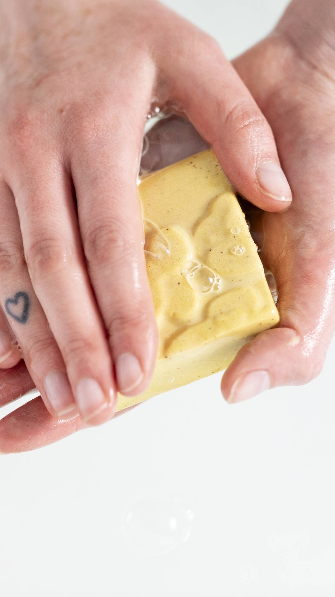 A close-up image of the model's hands on a white background as they gently lather up the Drop of Hope soap. 