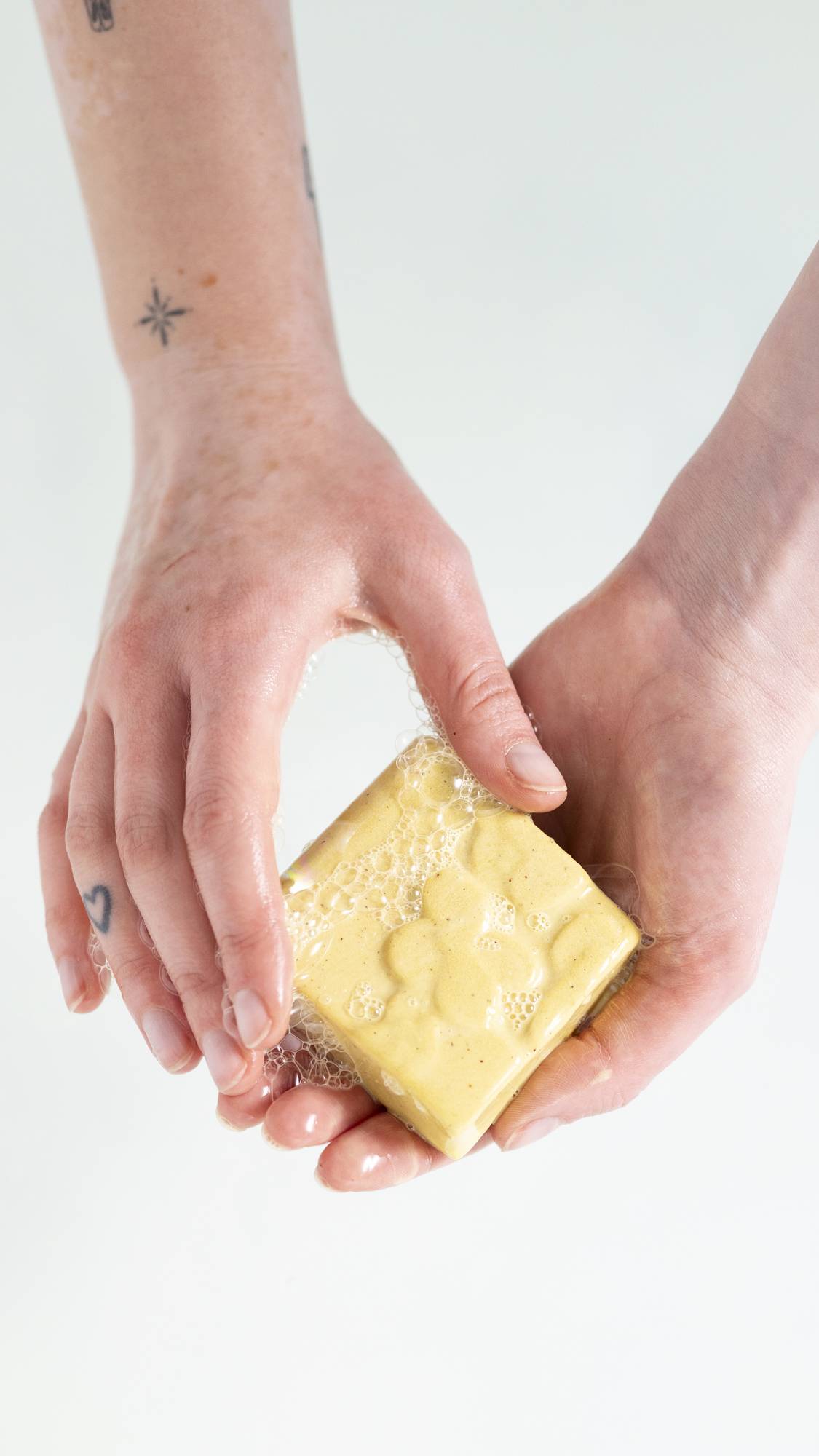 A close-up image of the model's hands on a white background as they gently lather up the Drop of Hope soap. 