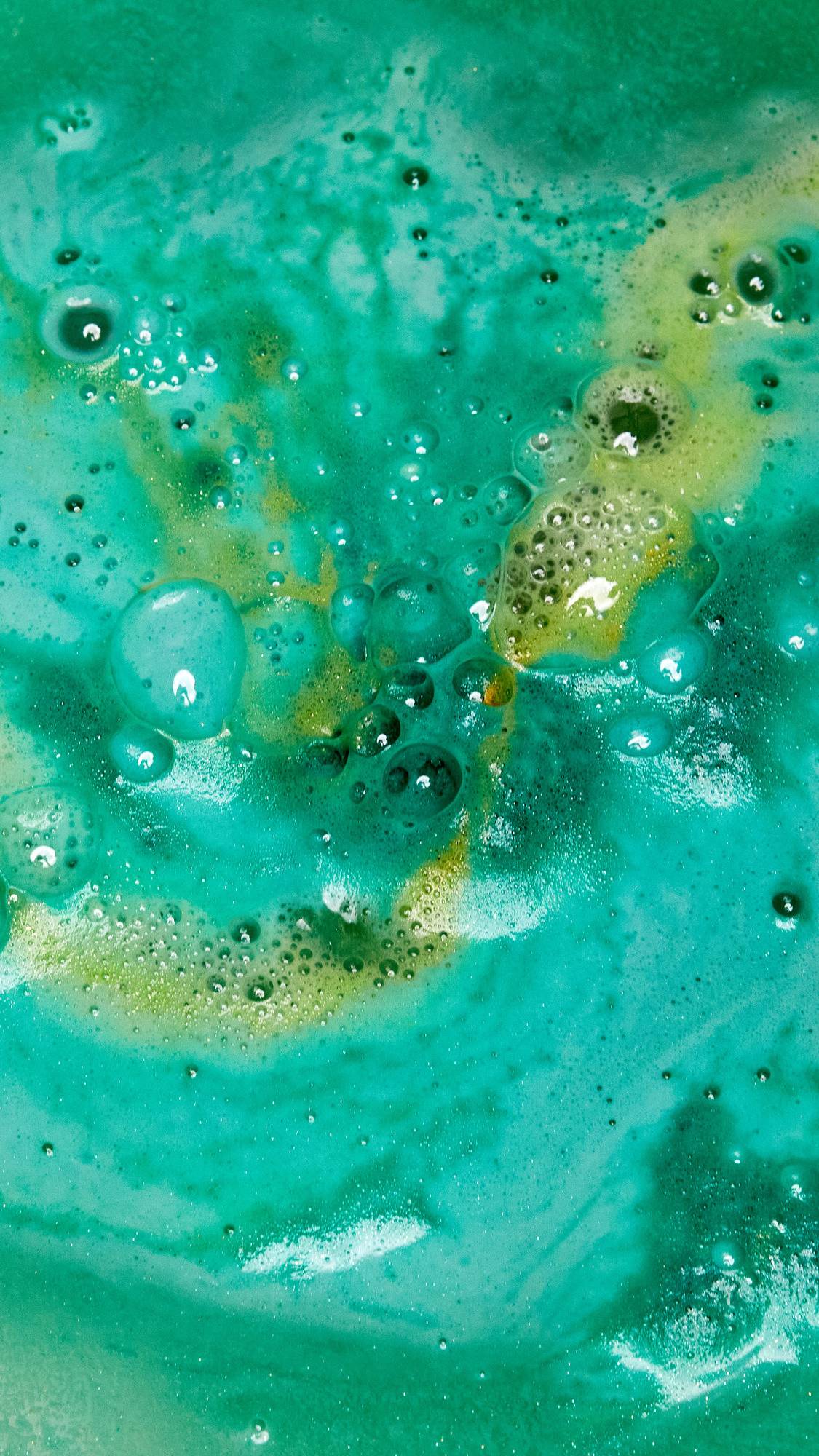 The Druid of Bath bath bomb is slowly dissolving leaving behind bubbly swirls of deep green and golden foam. 