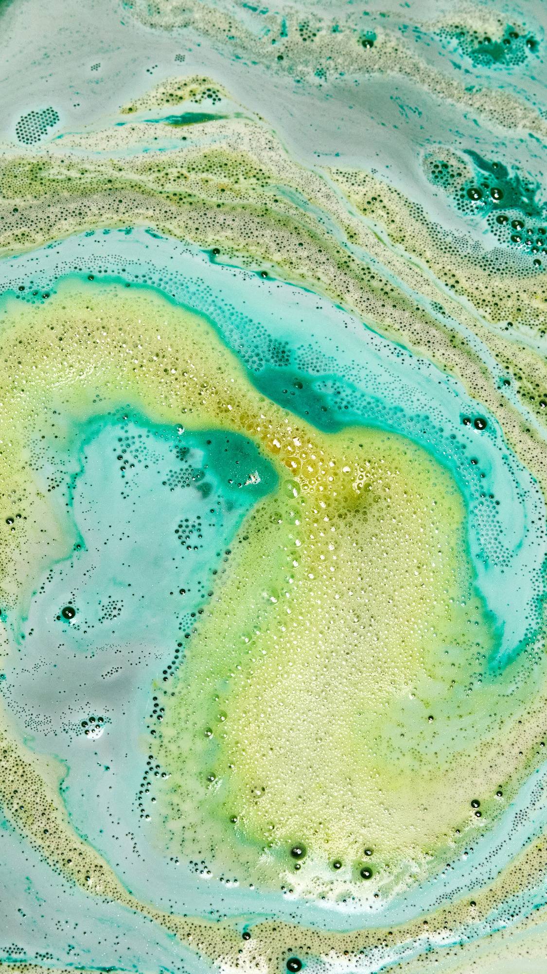 The Druid of Bath bath bomb is slowly dissolving leaving behind bubbly swirls of deep green and golden yellow foam. 
