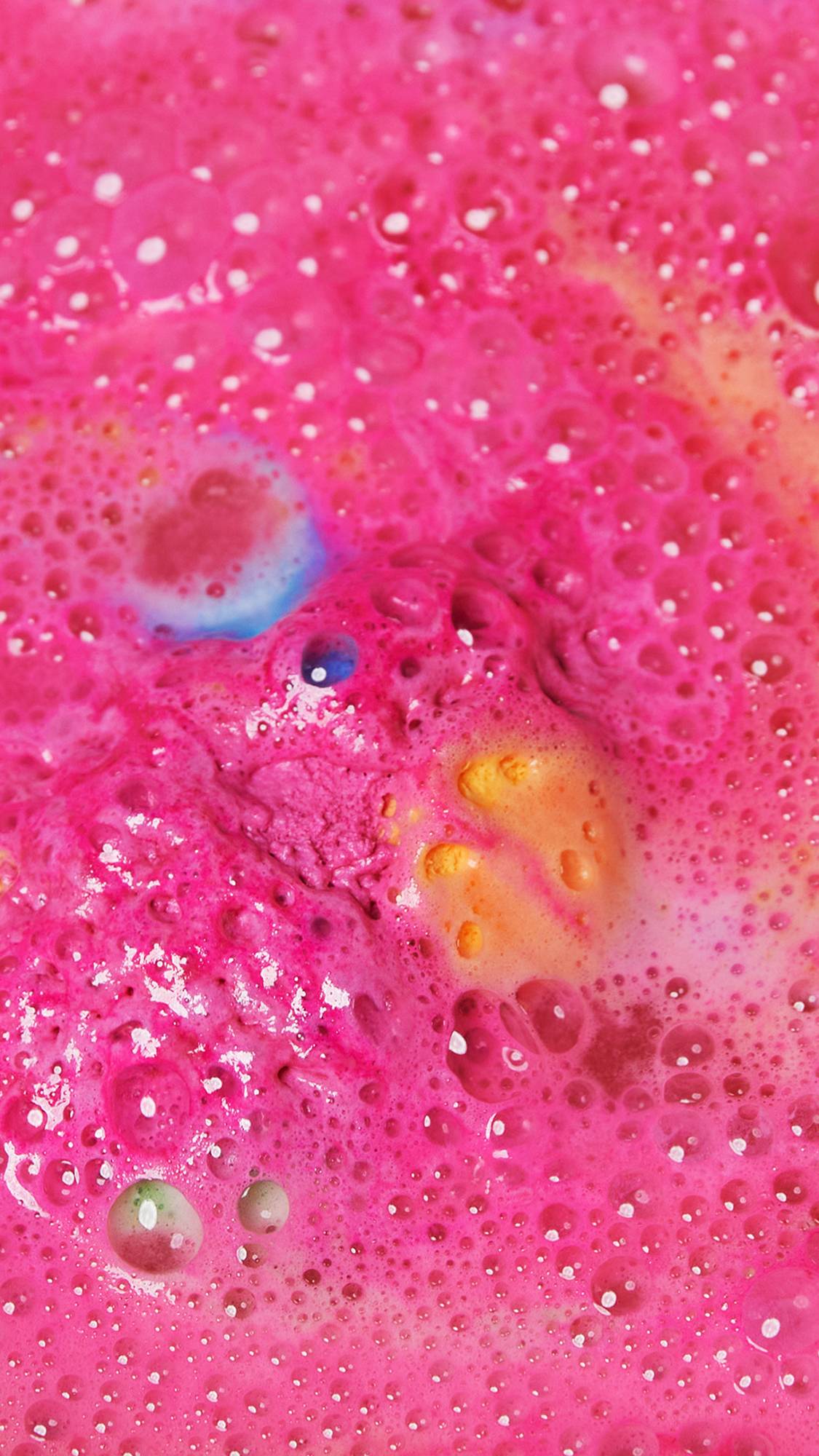 The pink, spotty egg part of the bath bomb has mostly dissolved leaving a thick, bubbling foam and pops of blues and yellows. 