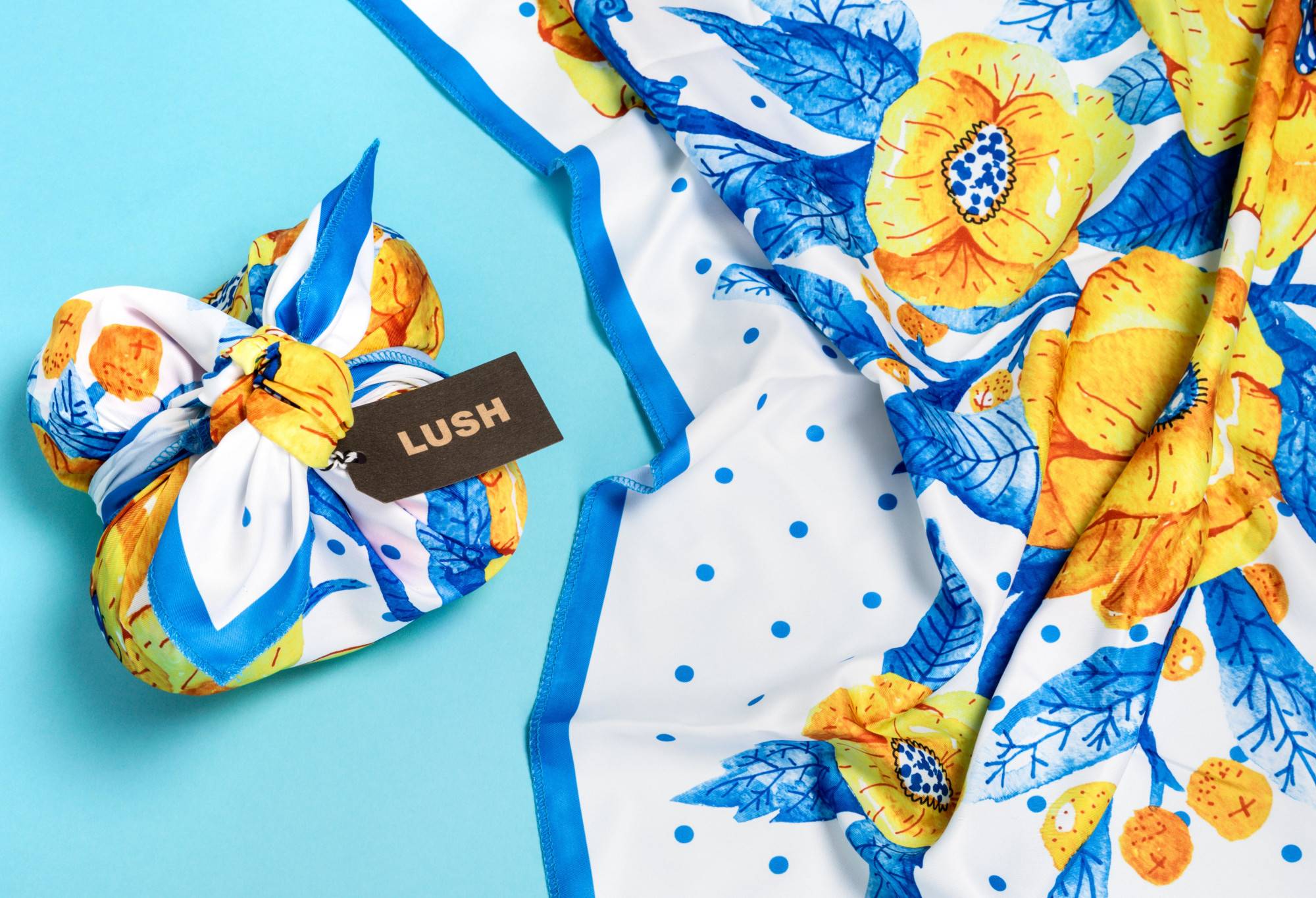 The knot wrap is wrapped around a rectangular box, as well as laid out flat, on a bright blue background. 