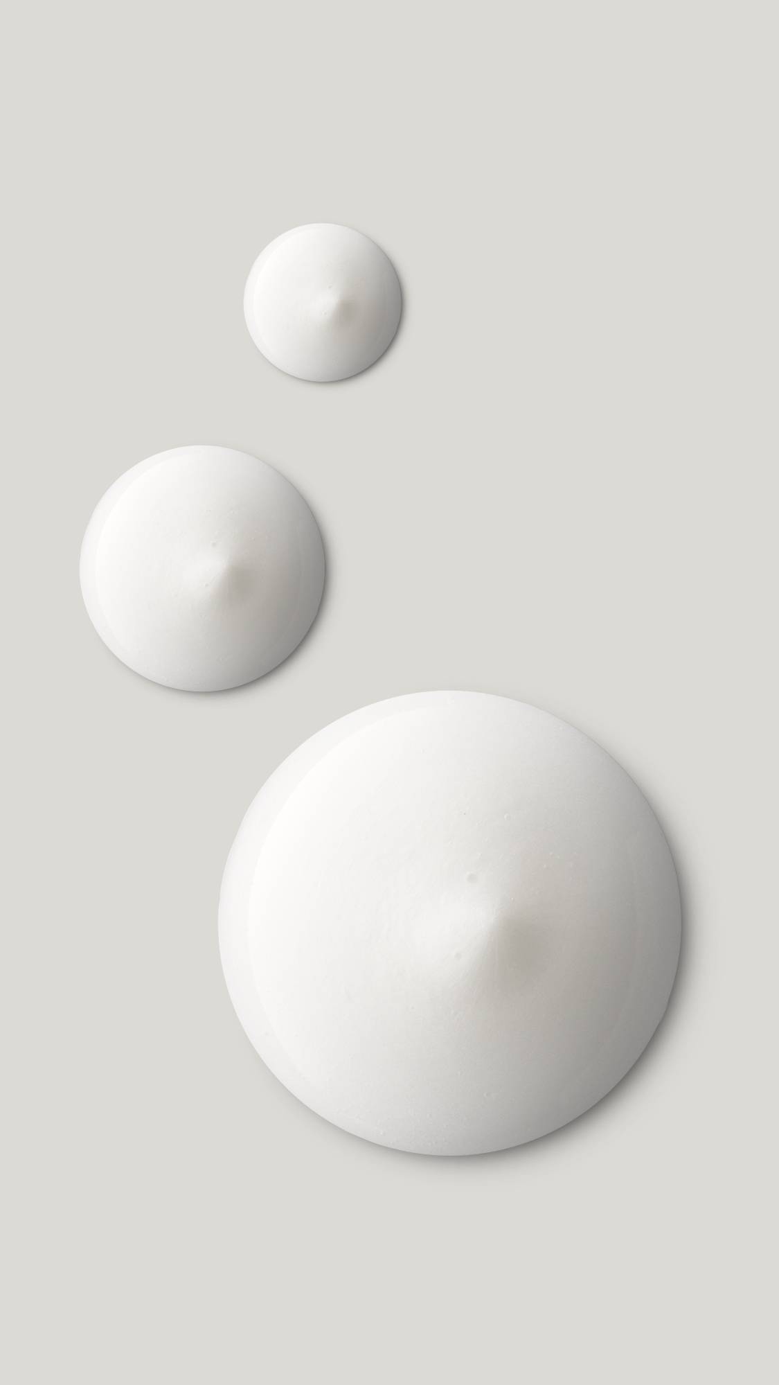 The image shows three circular product droplets getting larger. They are perfect circular swatches of bright white Enchanted eye cream. 
