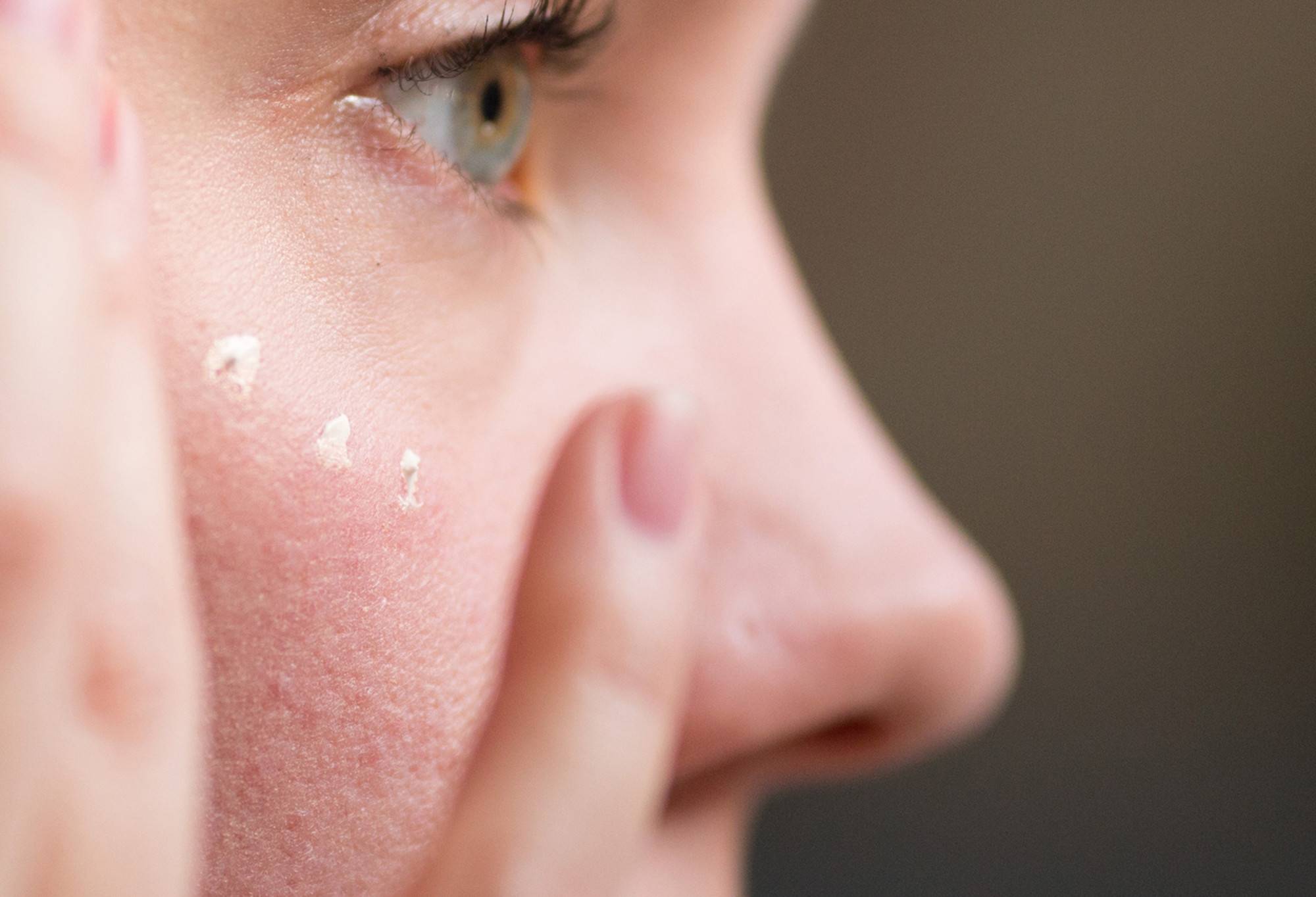 A close-up of a person dabbing tiny splotches of creamy, shimmery Feeling Younger skin tint at the top of their cheekbones.