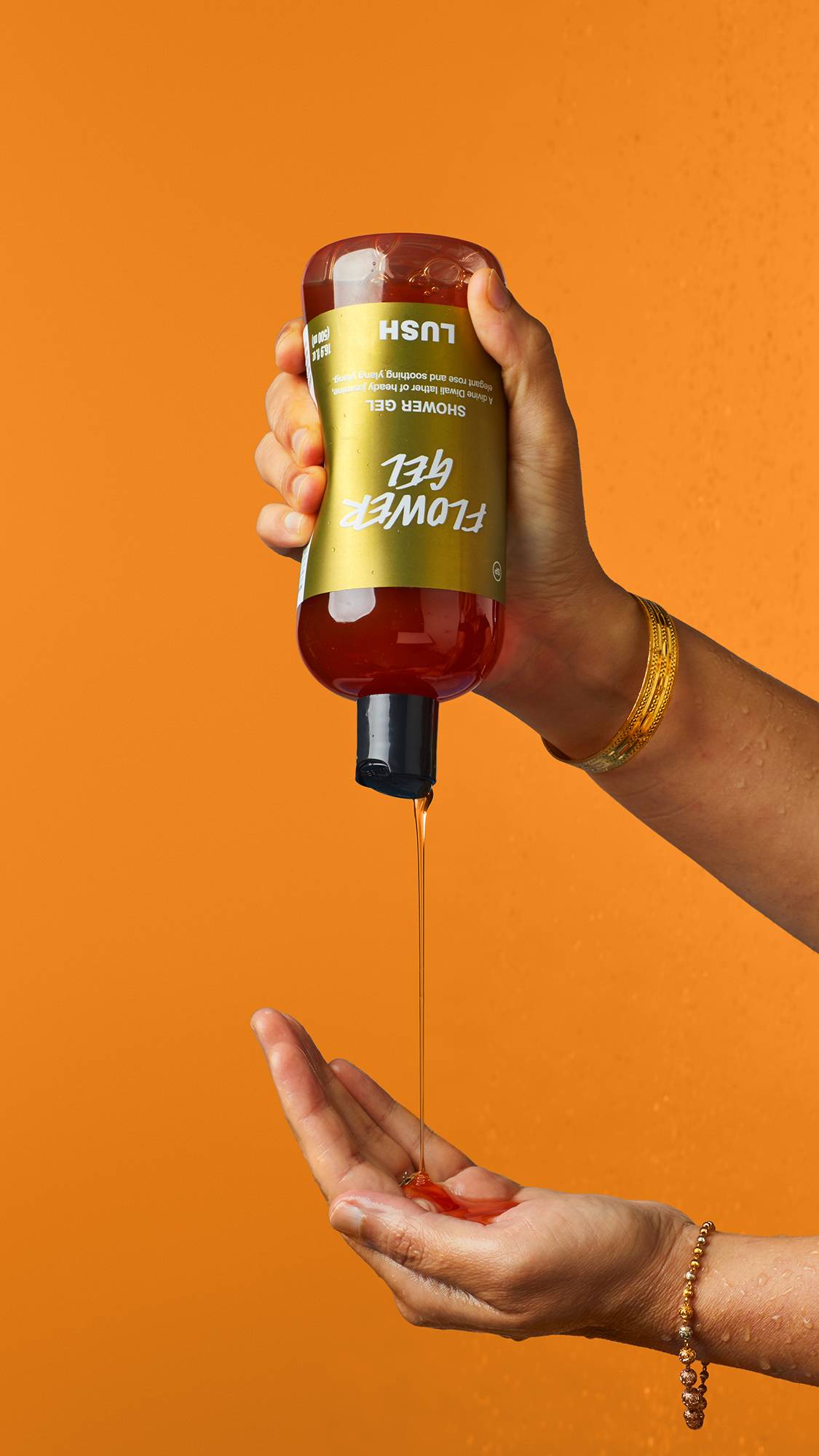 Image shows the model squeezing the Flower Gel shower gel out of the bottle into their hand on a bright orange backdrop.