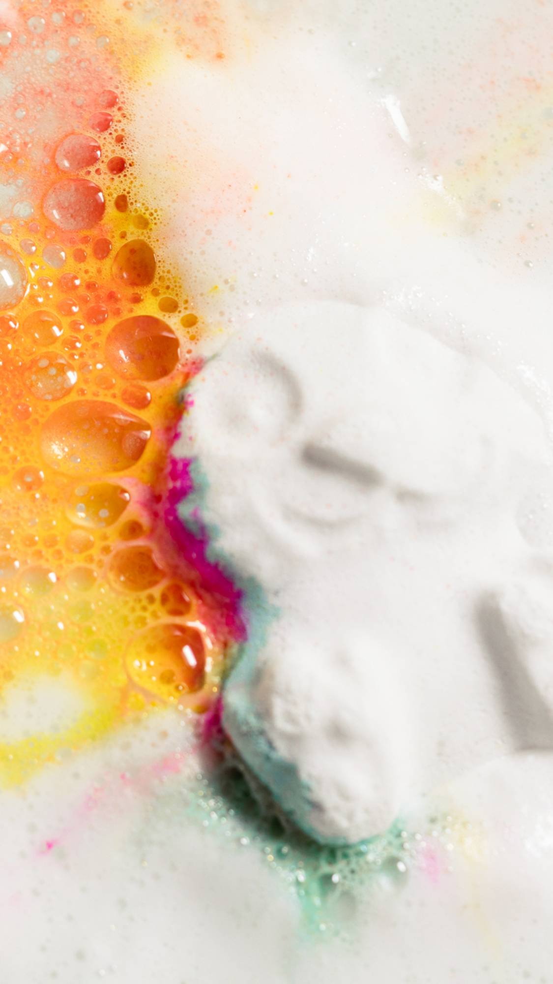 The Follow The White Rabbit bath bomb is dissolving in the bath water giving off thick white foam along with vibrant pink, orange, yellow and blue.