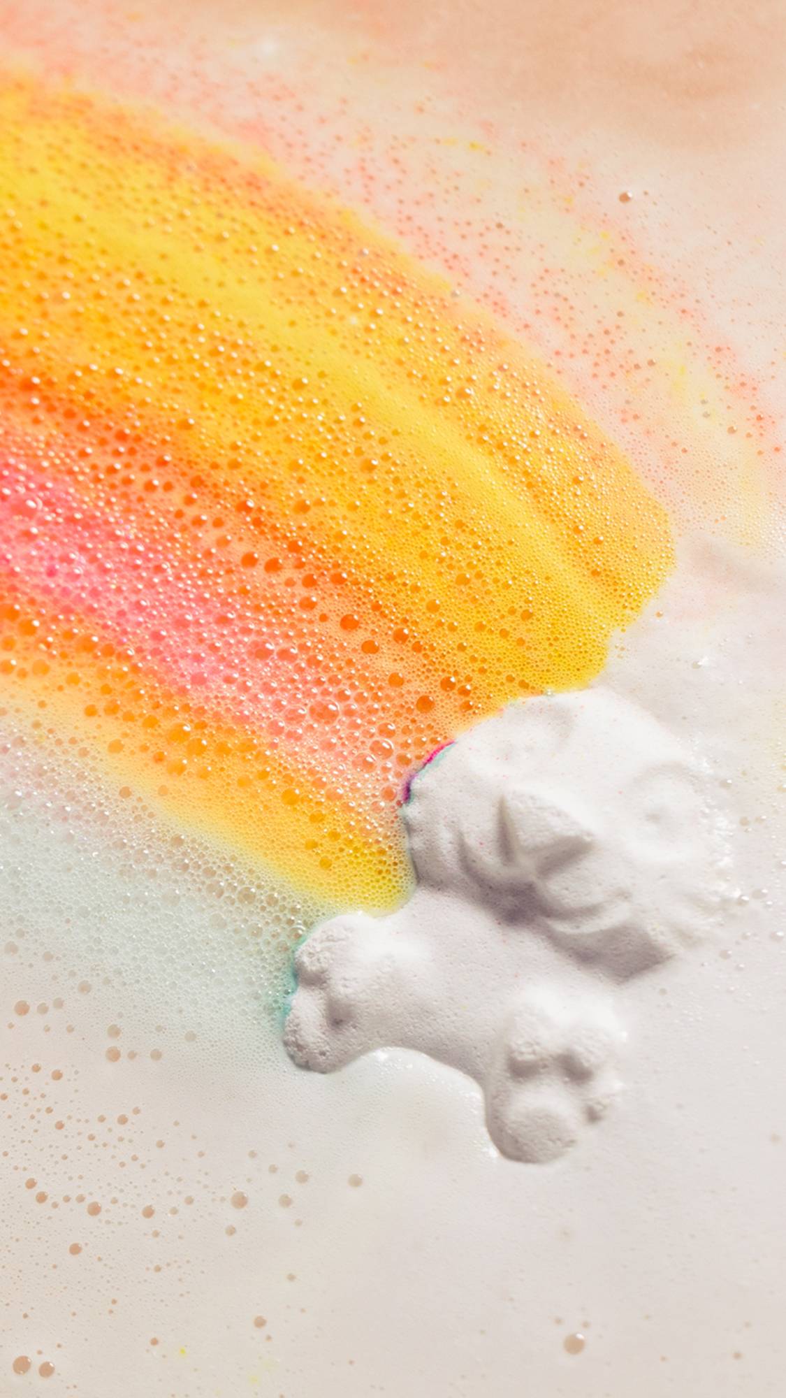 The Follow The White Rabbit bath bomb is dissolving in the bath water giving off thick white foam along with vibrant pink, orange, yellow and blue.