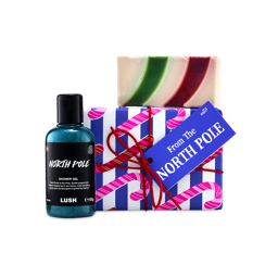 A Lush "From The North Pole" gift set wrapped in blue and white candy cane paper with a blue tag, flanked by a bottle of blue shower gel and topped with a red, green, and white striped soap