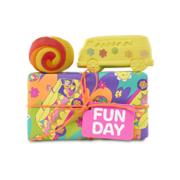 Fun Day. A rectangular gift box decorated in colourful paper with a yellow school bus design with disco balls and flowers, tied with an orange string and tag. Two included bath products sit on top of the box. 